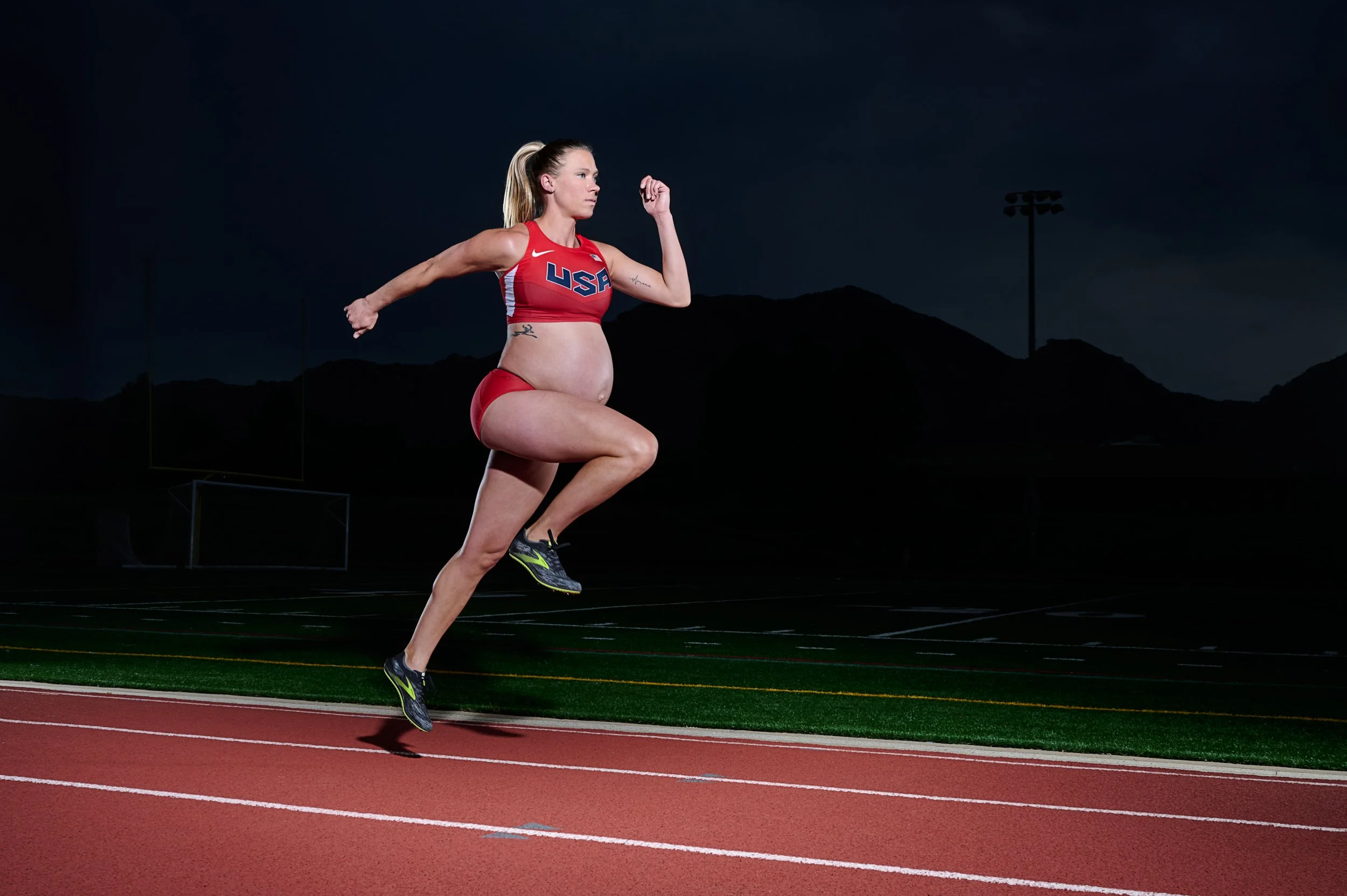 Sprinter driving down the track under stadium lights, bare bump, red racing crop top.