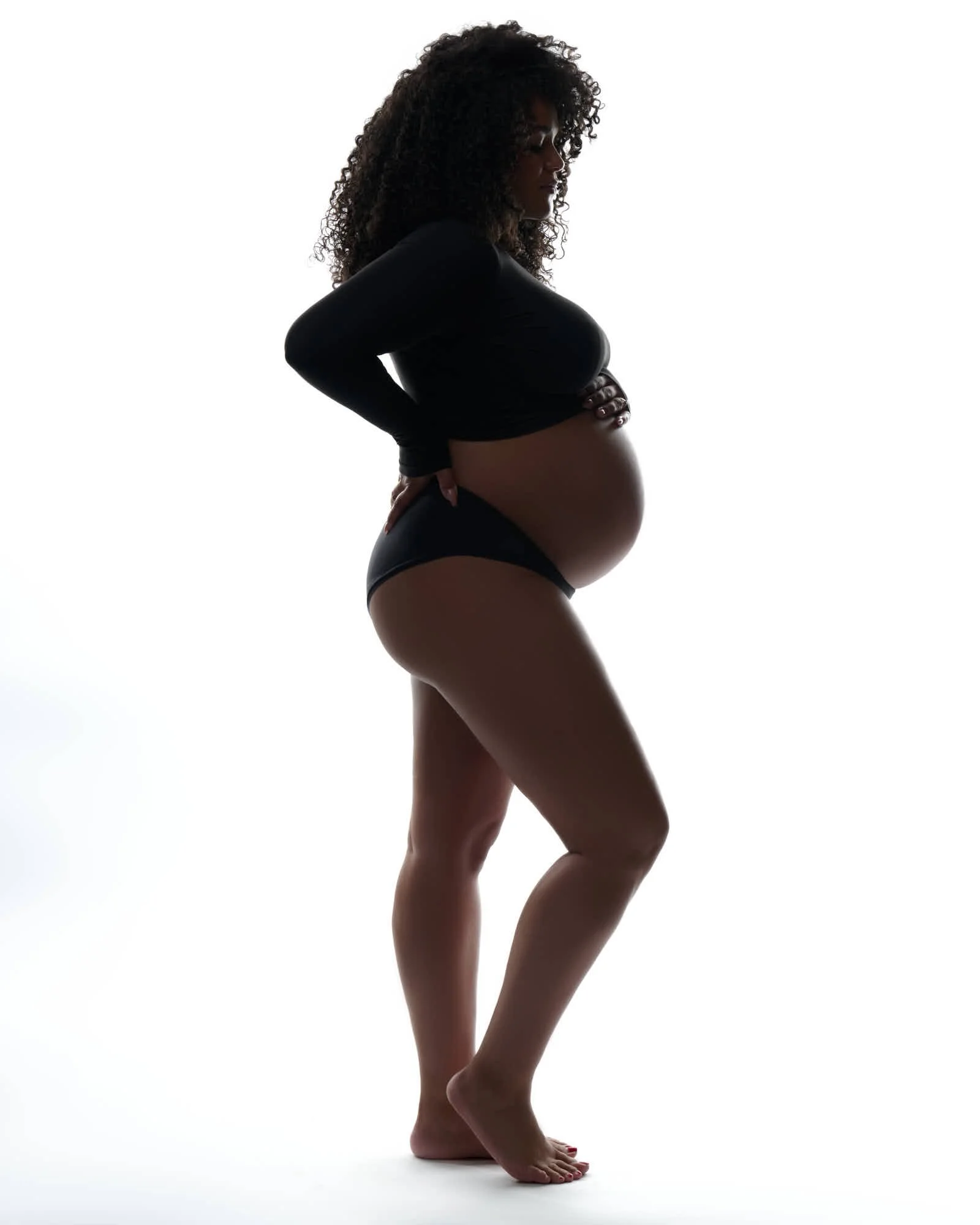 Black crop top and briefs in profile, curls loose against a white backdrop.