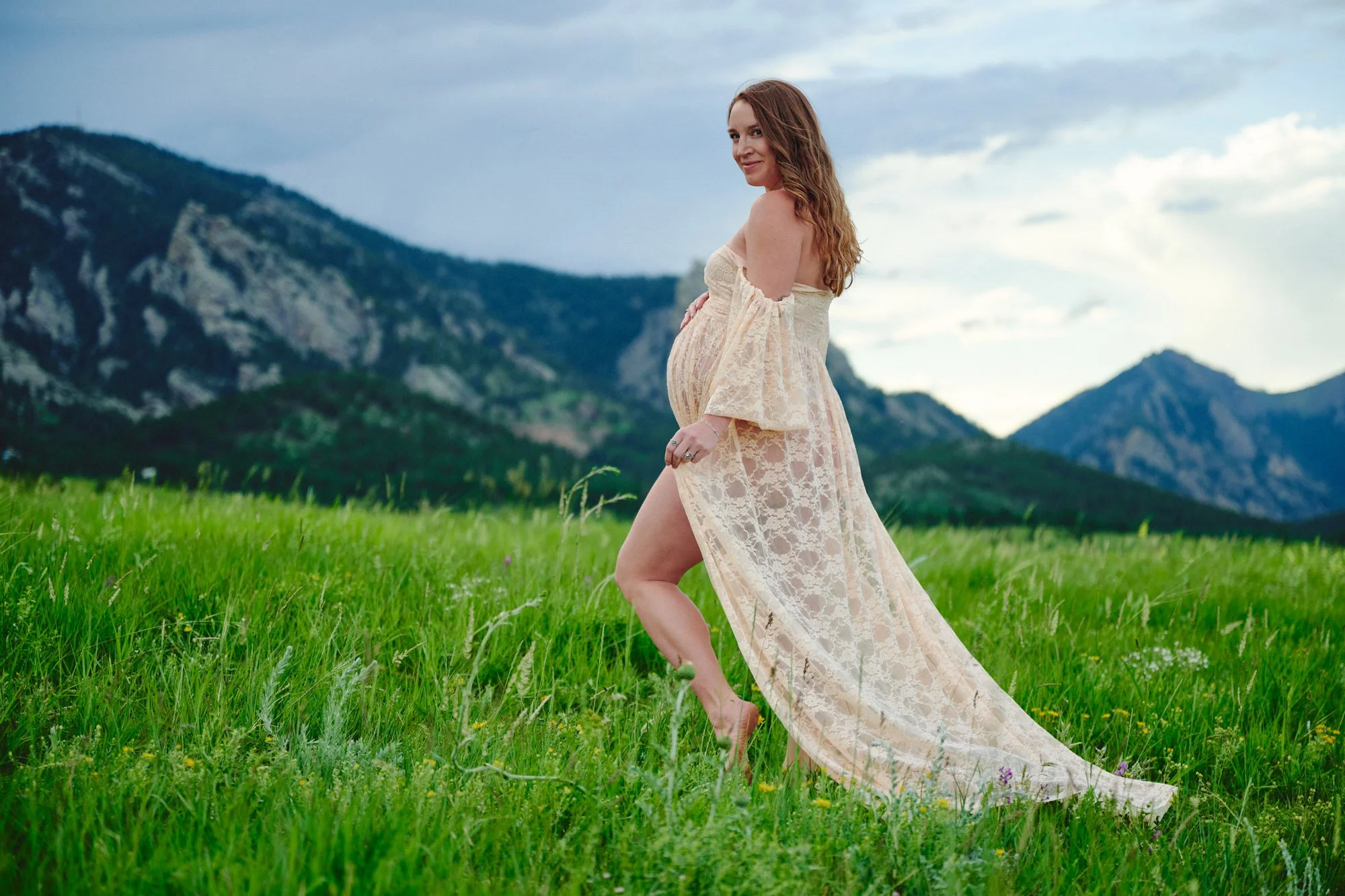 Pregnant mom standing in a bright green field with Colorado front range behind her.