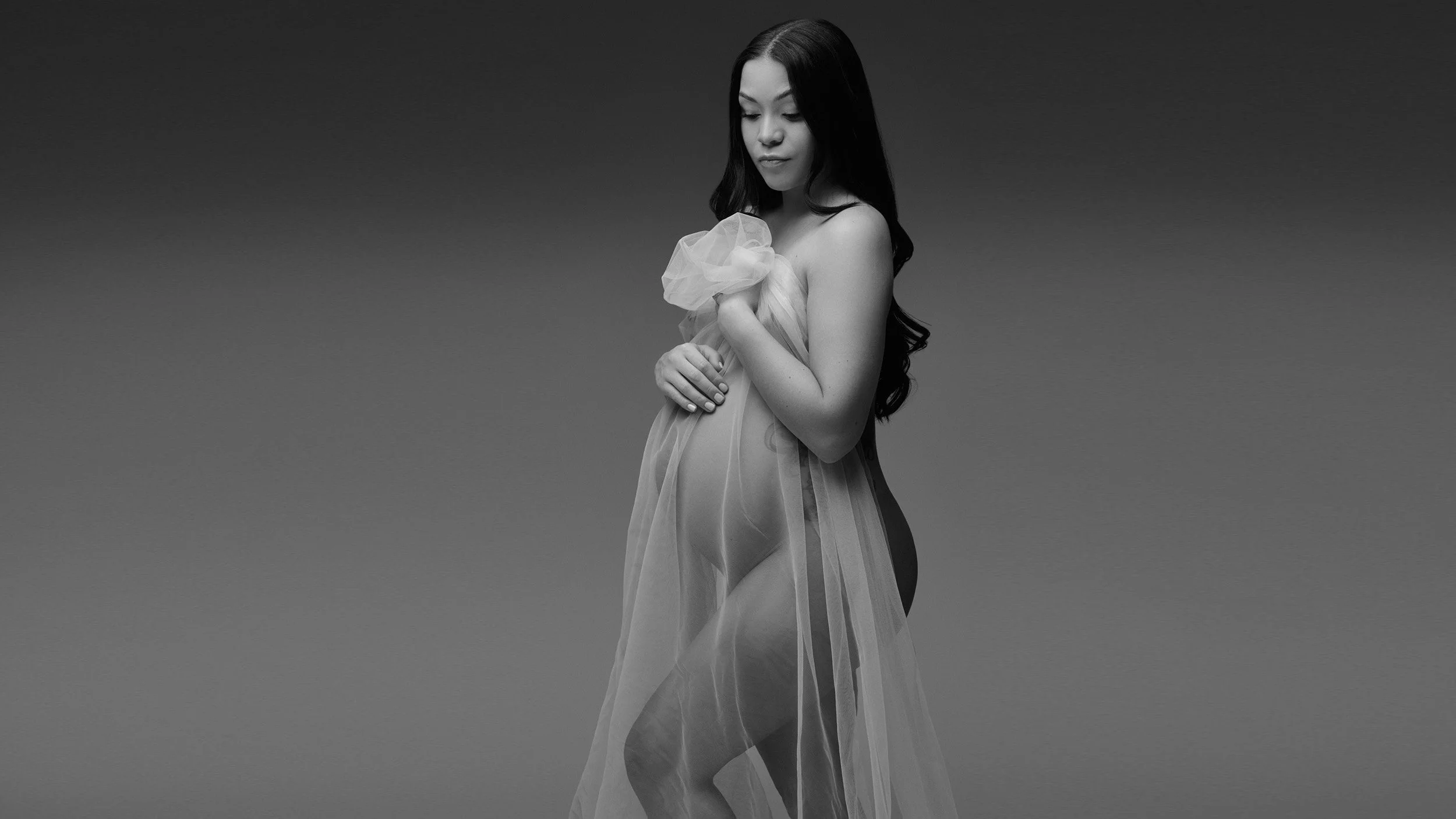 Black and white photo of a woman with long dark hair, wearing a sheer, flowing fabric dress, with her eyes closed.