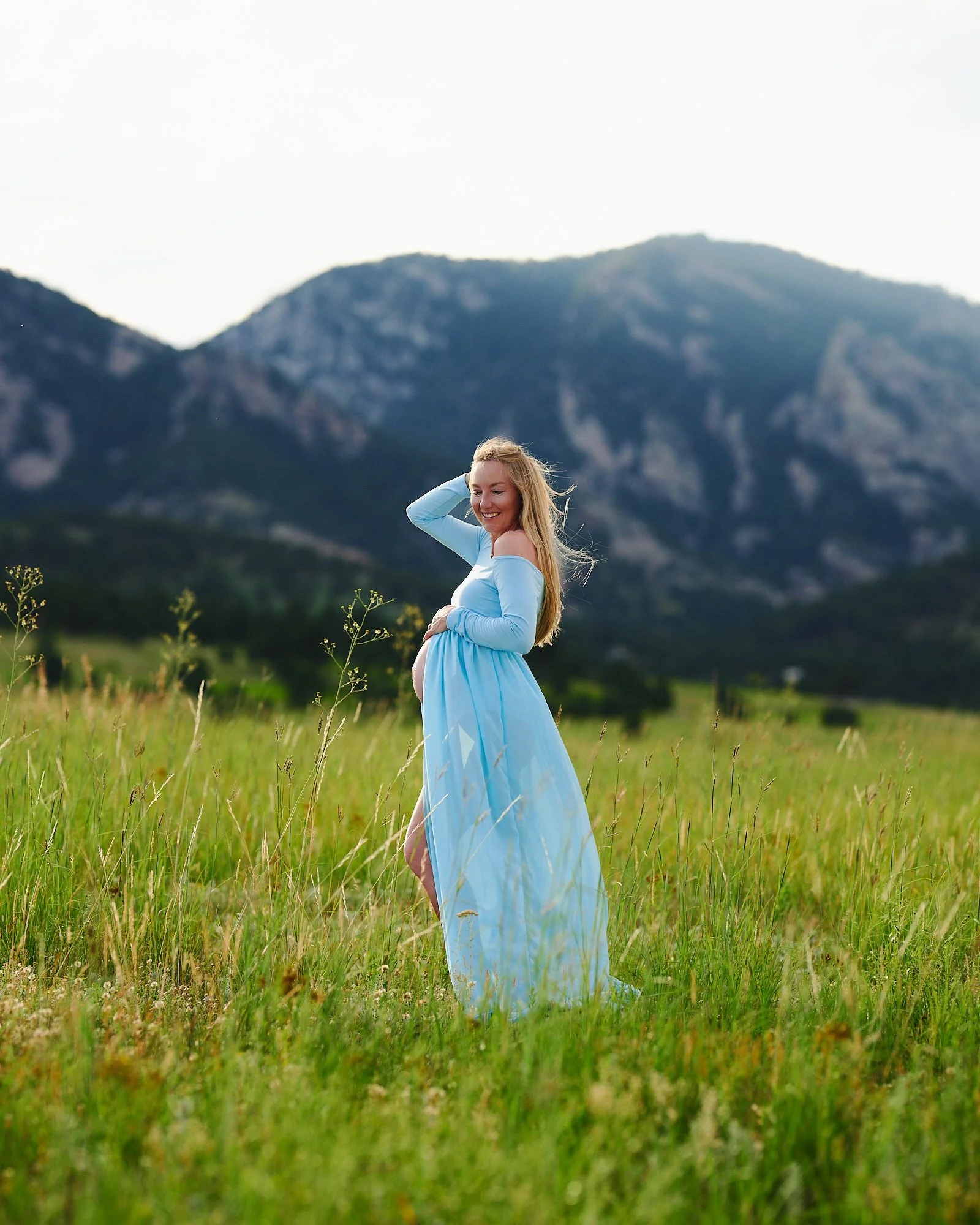 Mother to be in a flowing light blue maternity gown, backlit in a summer meadow.
