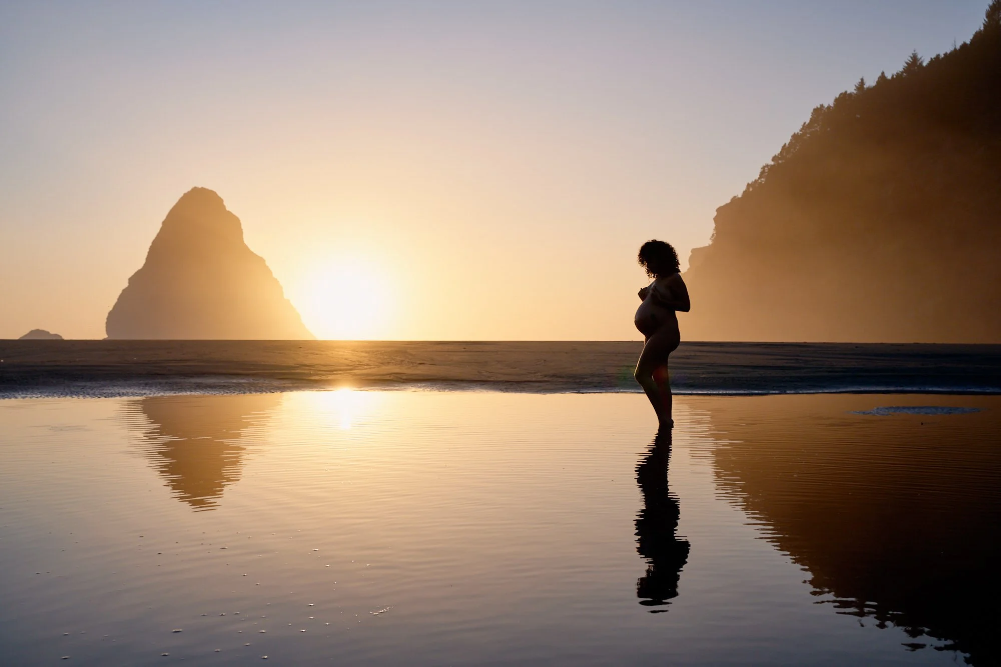 Silhouette on the tide flats at sunset, a sea stack and her reflection in the wet sand on the Oregon coast.