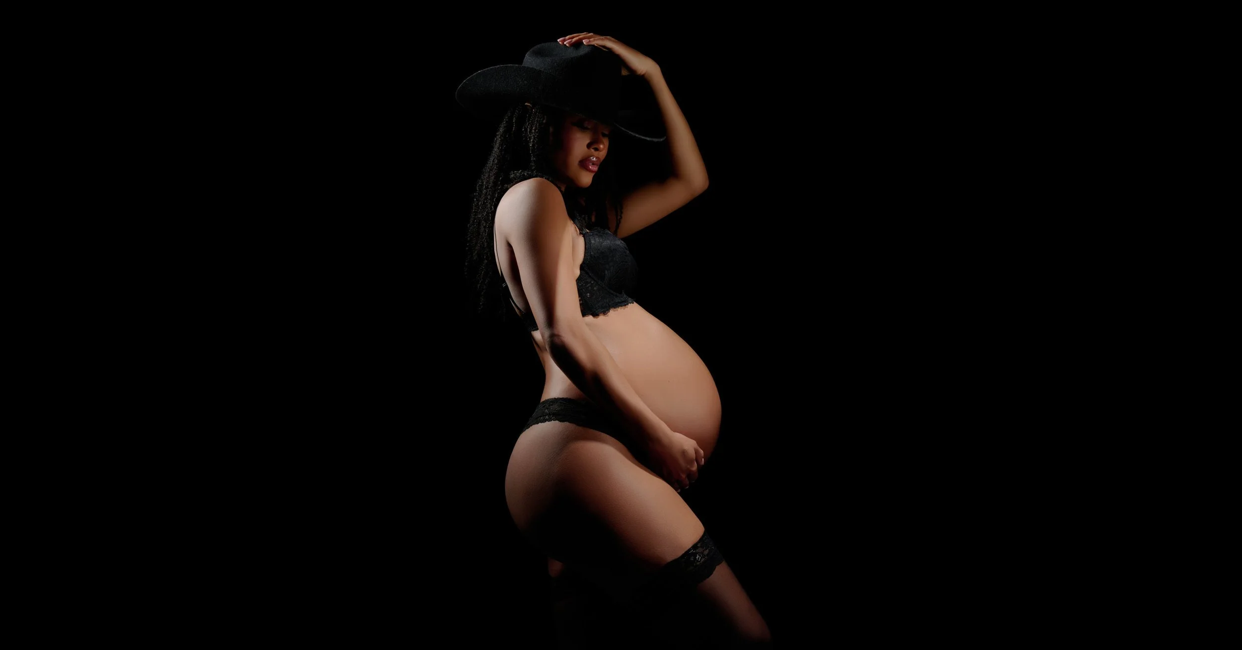 Sheer black bodysuit in low-key light, one of the boldest maternity photoshoot outfits.