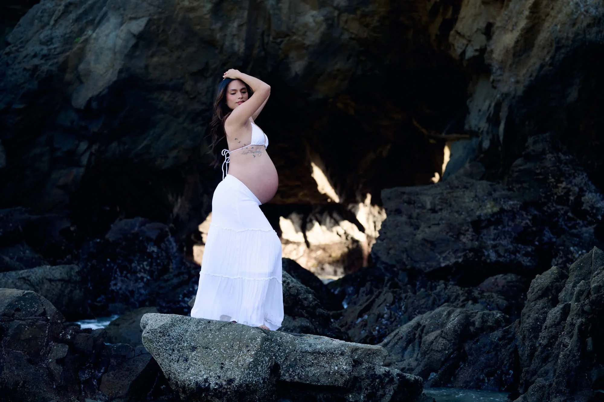 White skirt on a boulder at the mouth of a sea cave, sunlight breaking across the rock.