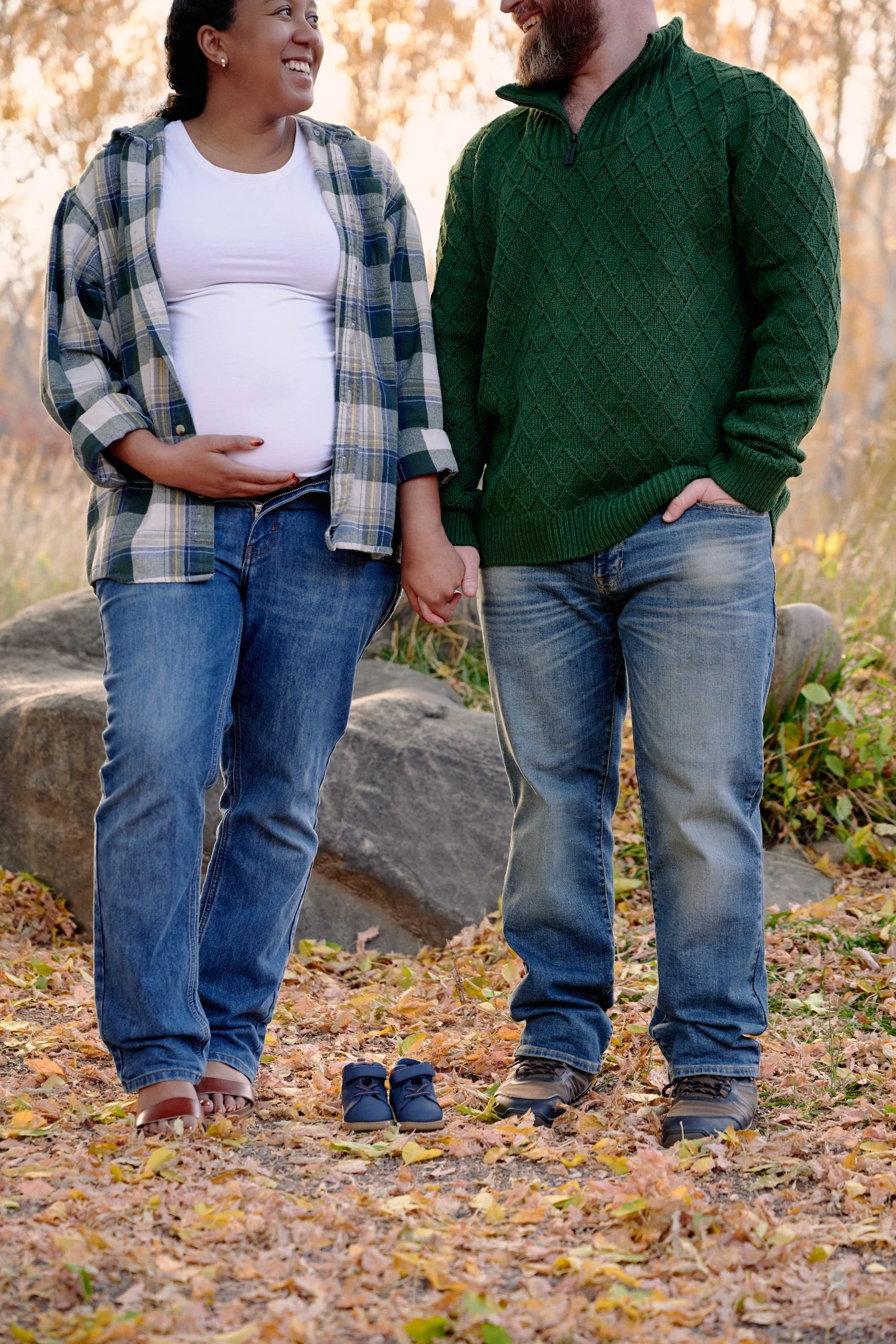 Green plaid and cozy sweaters on a boulder, tiny baby shoes set between them.