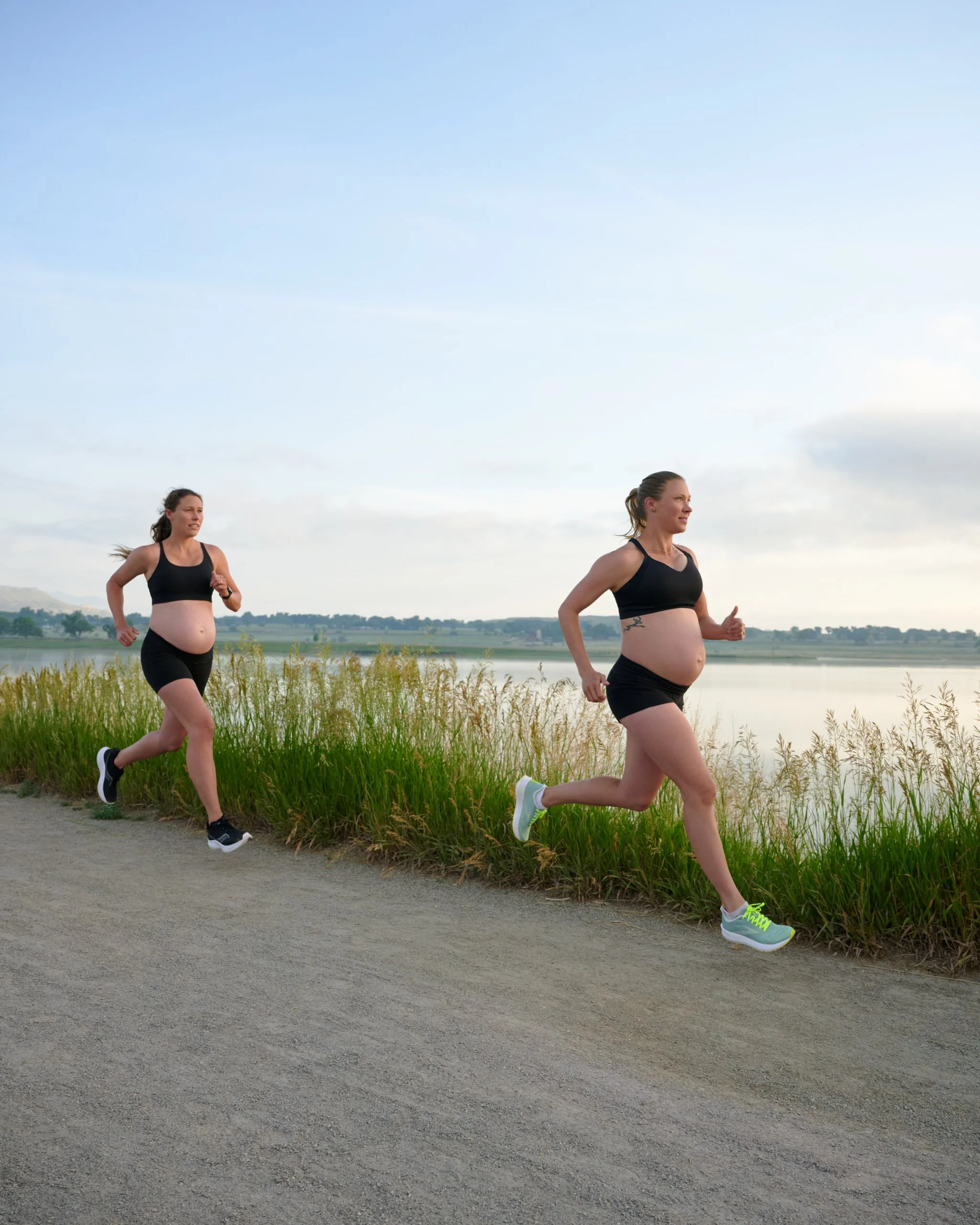Two expecting runners stride together along a lakeside path, panned in soft motion blur.
