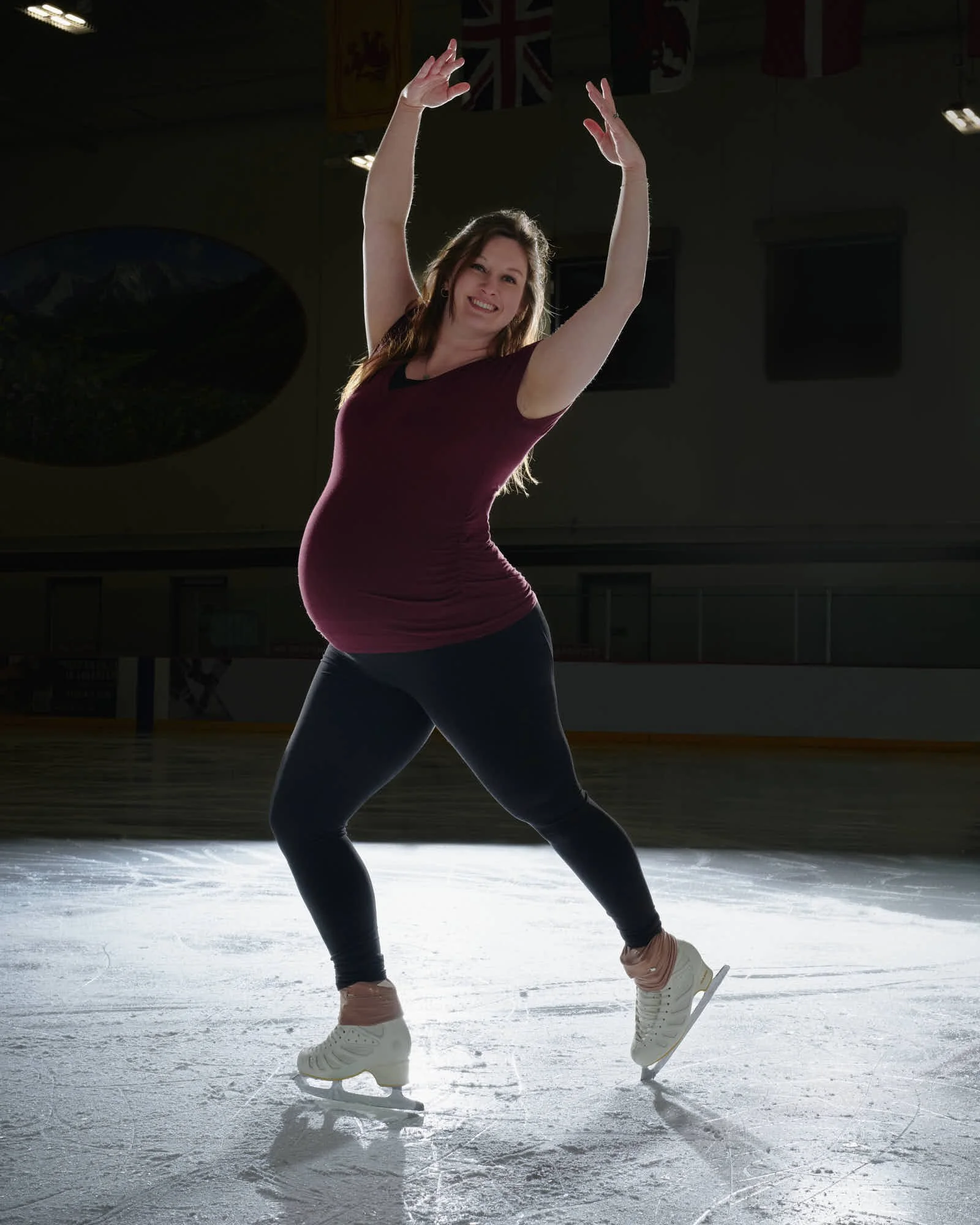 Landing pose with arms overhead, ice spray settling, empty seats beyond.
