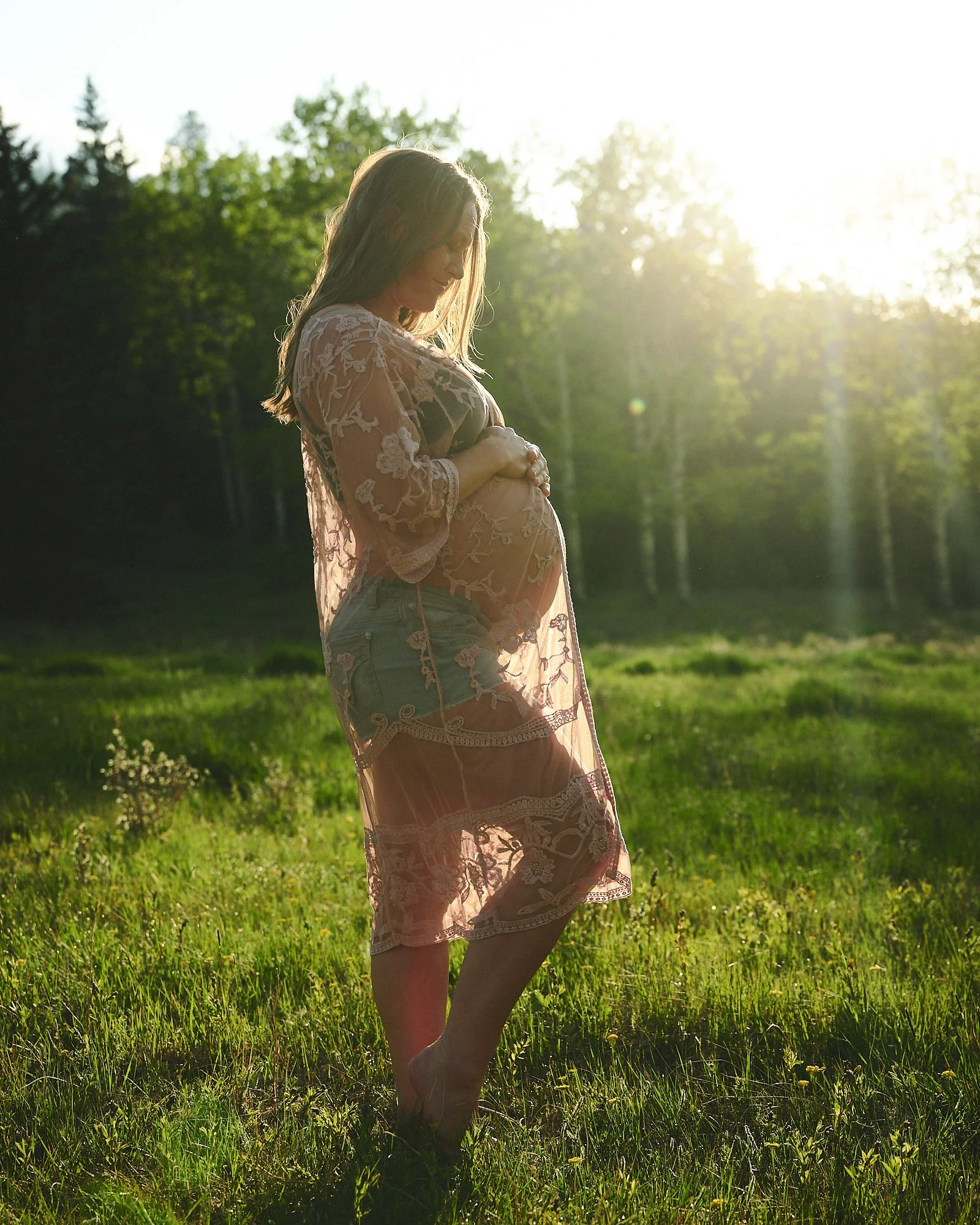 Backlit in a sheer floral robe, evening sun flaring through the forest behind her.