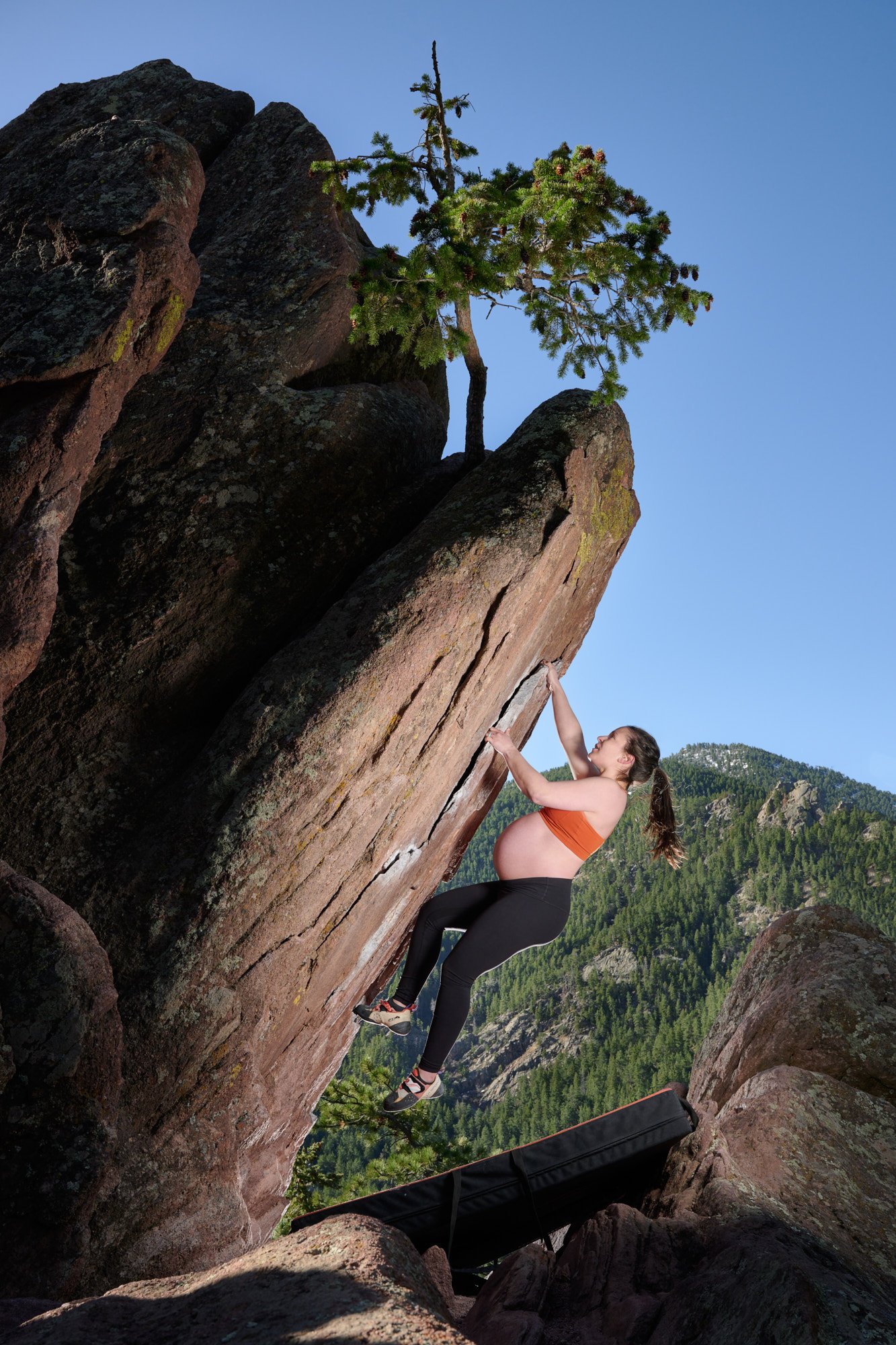Pulling through a red sandstone bulge in an orange top, blue sky over the ridge.