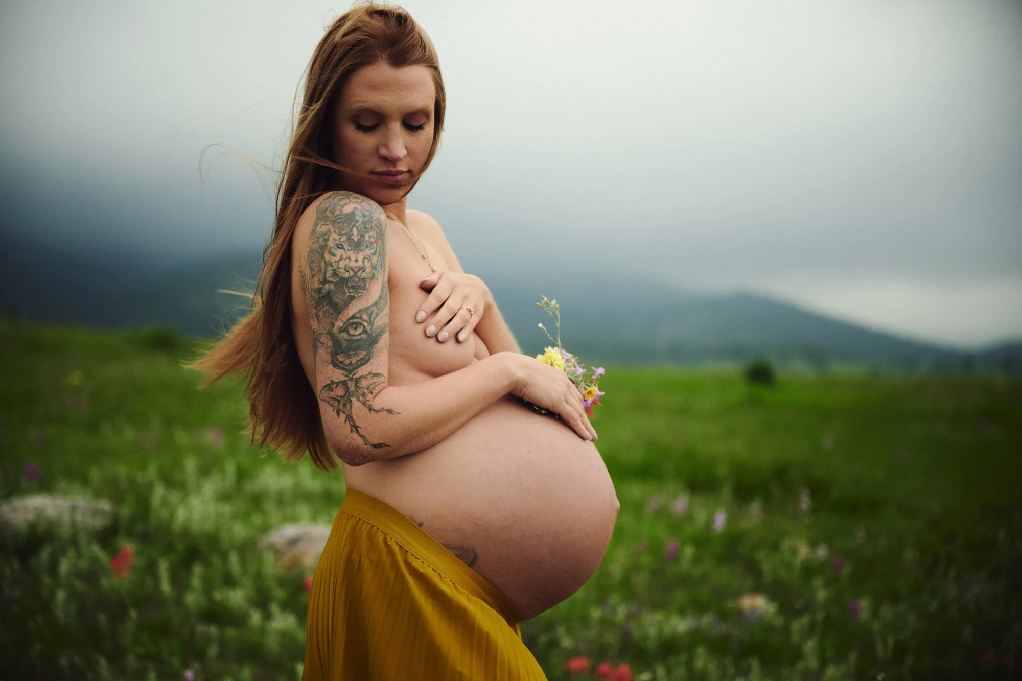 Expecting mother at 39 weeks cradling her bare bump among Colorado wildflowers in misty light.