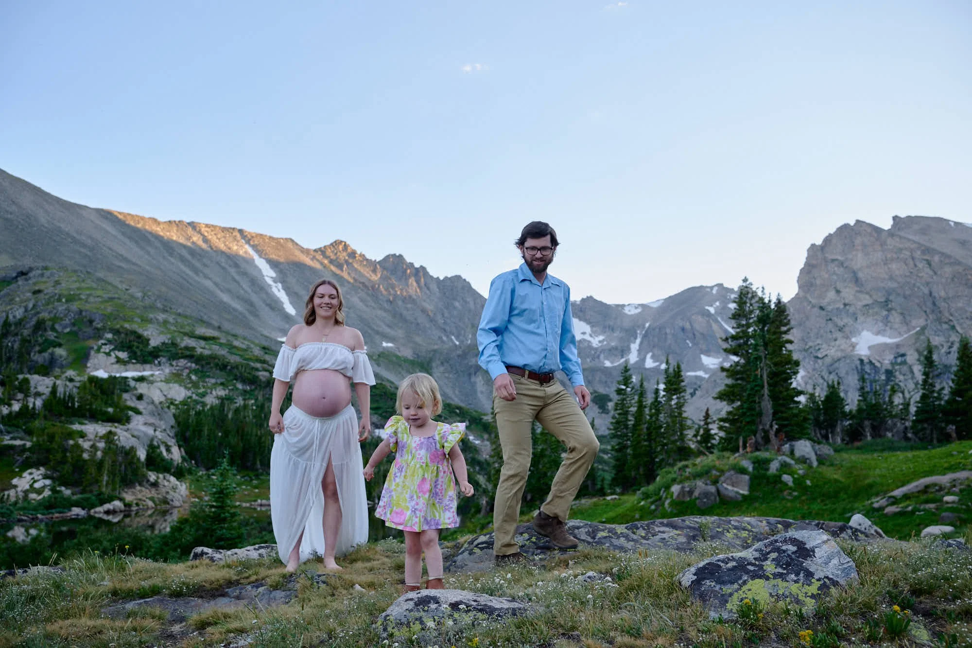 Family of three in a rocky alpine meadow on the Lake Isabelle trail, the Indian Peaks behind.