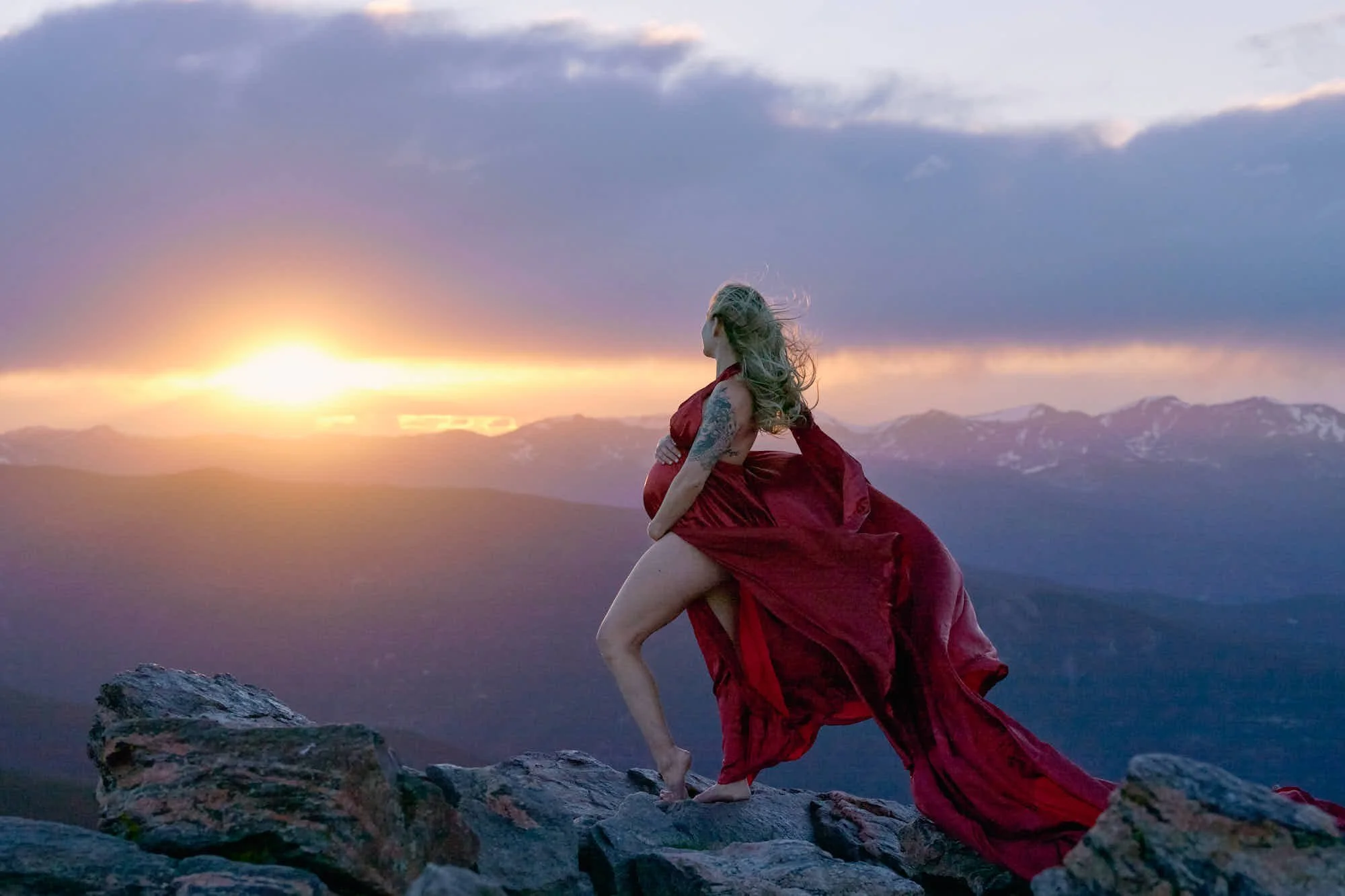 Red gown on the summit rocks of Chief Mountain as the sun sets behind Mount Blue Sky.