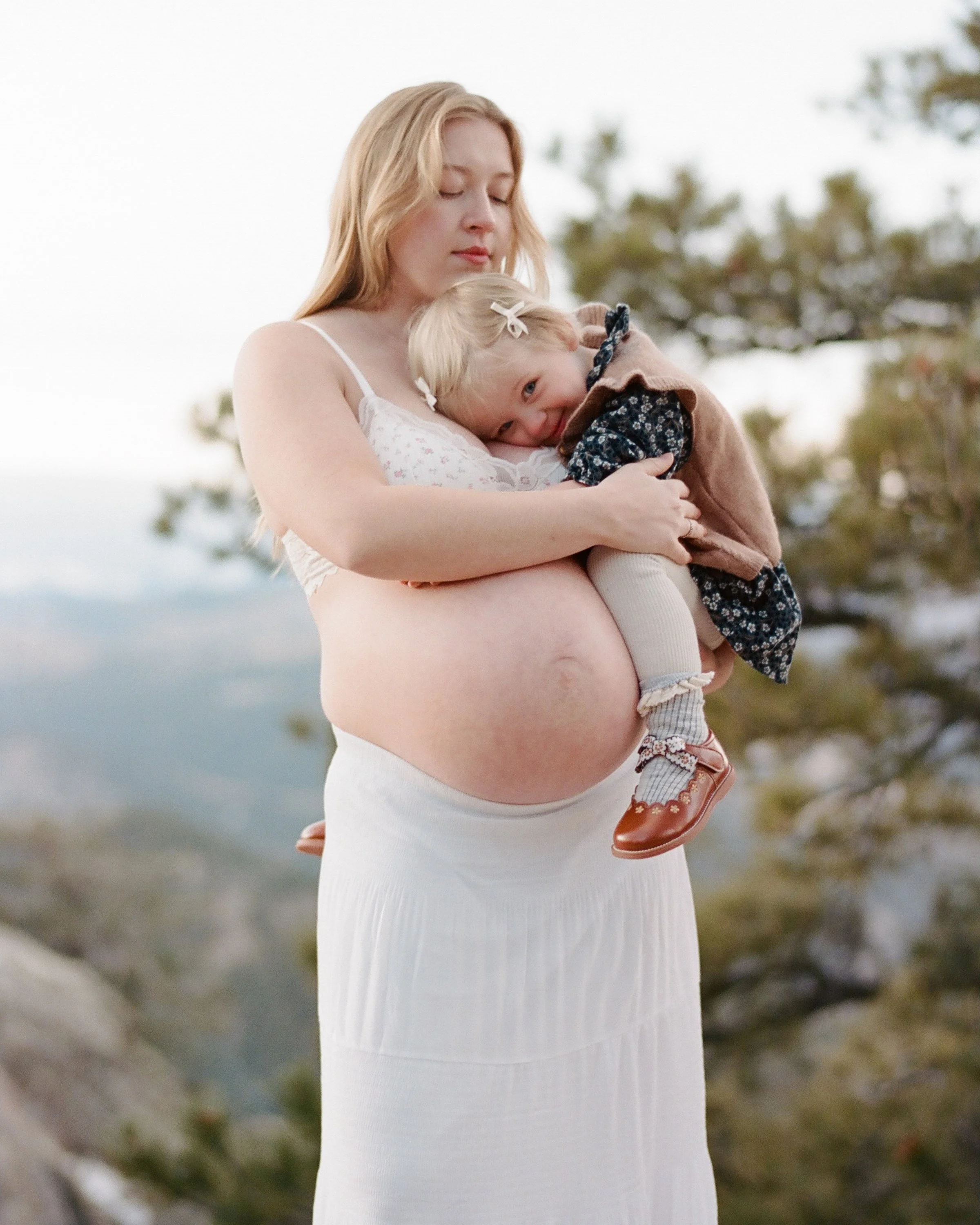 White gown on a rocky overlook, toddler on her hip and the range falling away behind them.