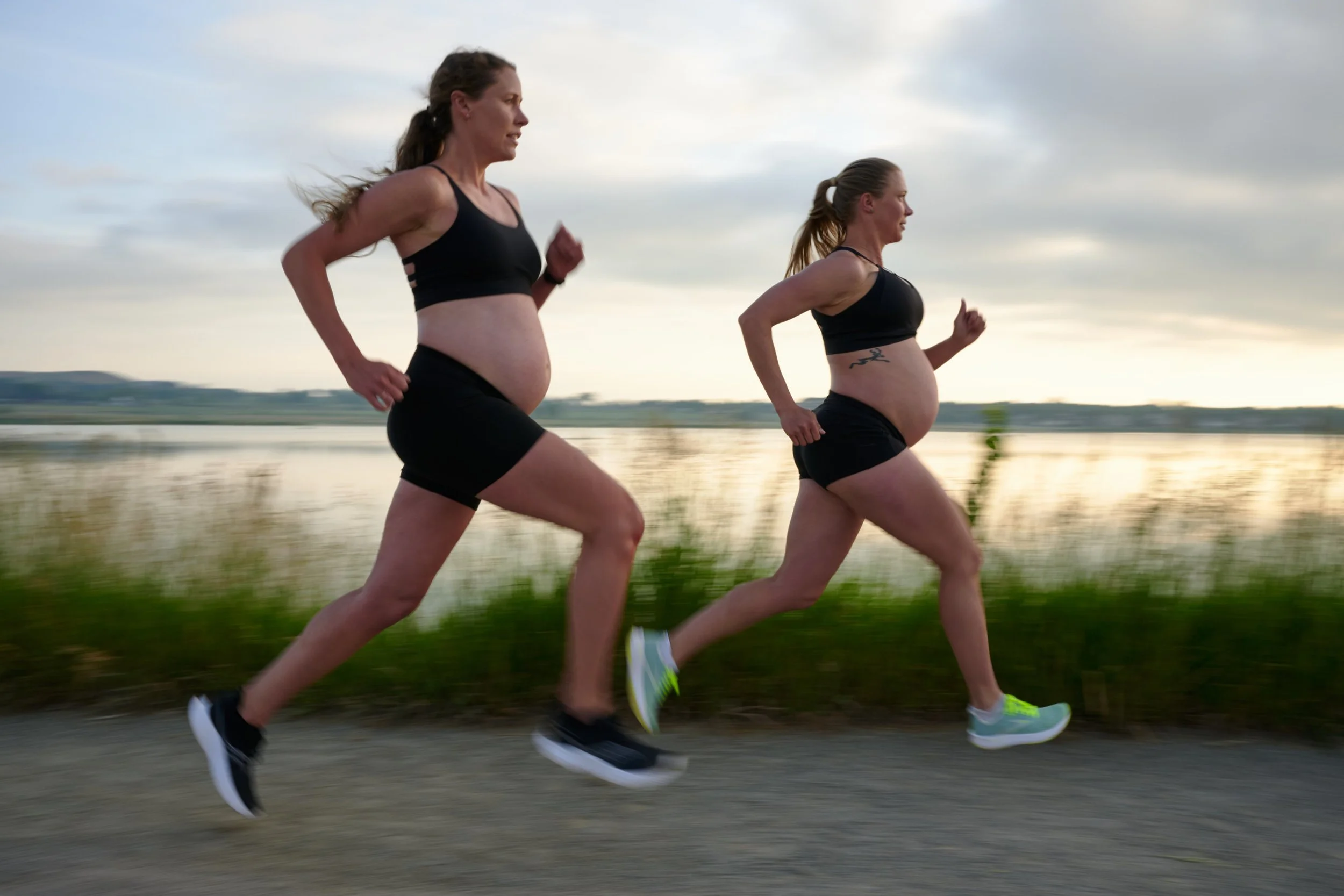 Pregnant runners in black mid-stride along a lakeside path, Outside Magazine Story.