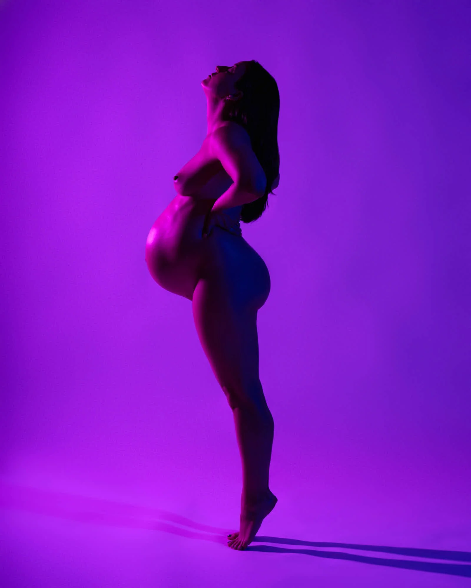 Bare form on tiptoe against saturated purple, one arm reaching overhead in a long clean line.