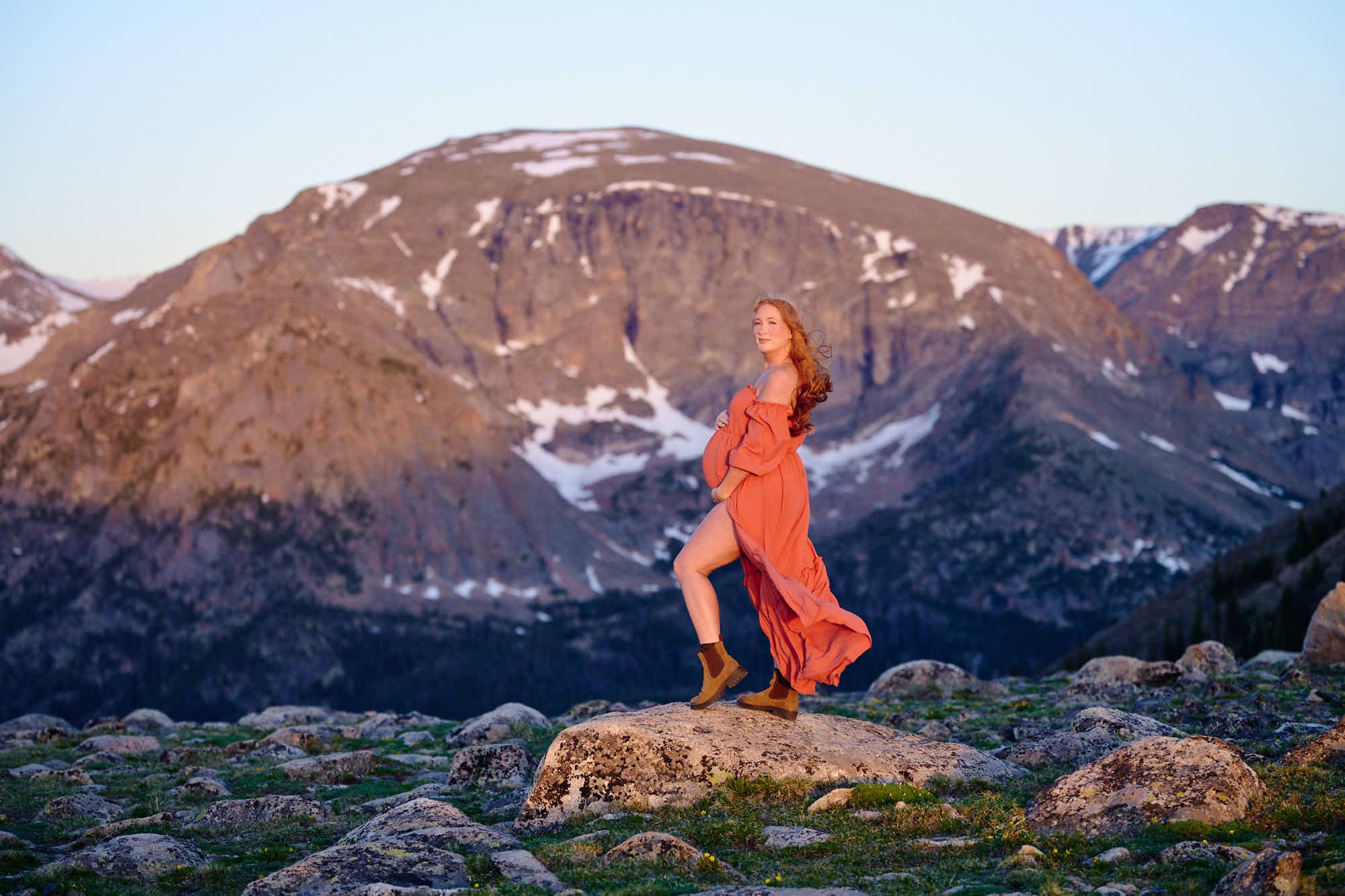 Striding across alpine tundra in a terracotta gown and lug-sole boots at sunrise.