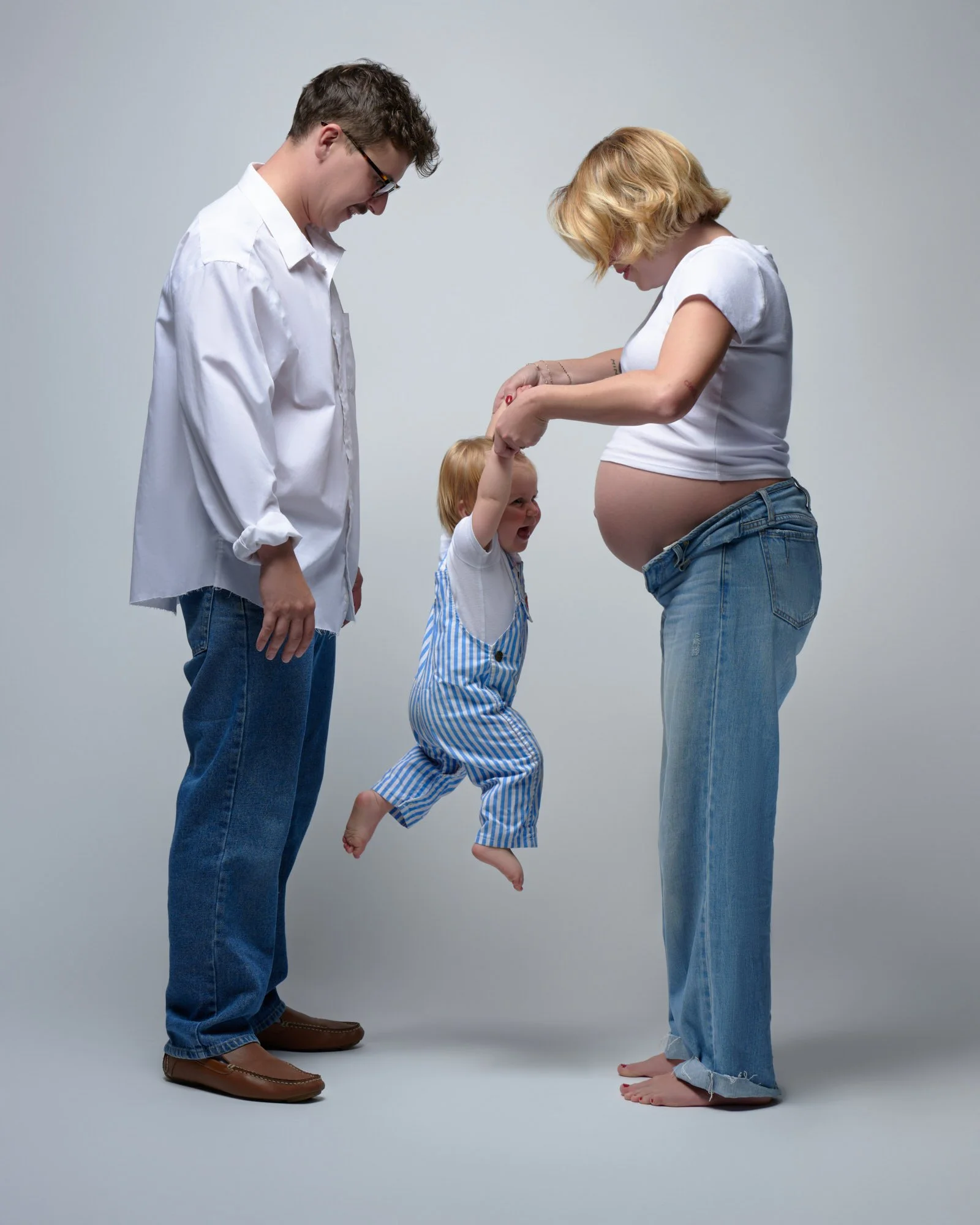 Swinging a giggling toddler by the hands during a casual studio maternity session.