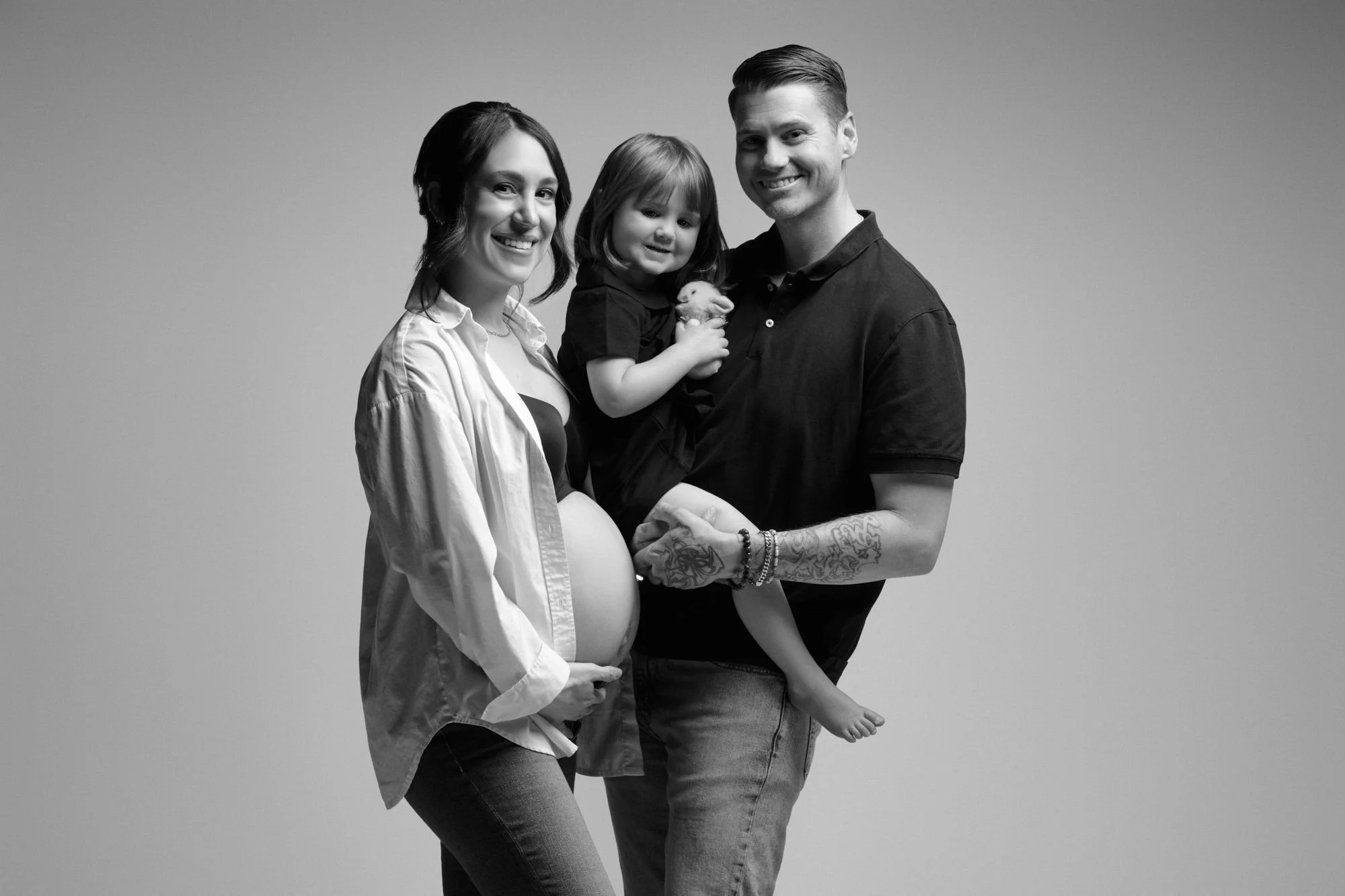 Family smiles together in the studio, dad holding their toddler close.