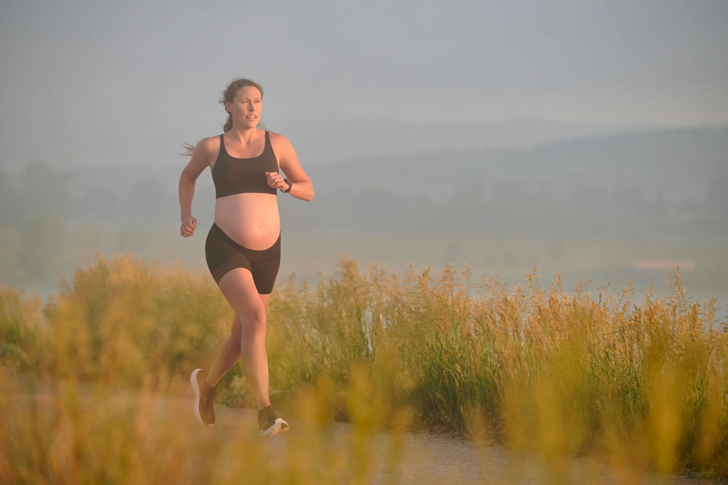 Pregnant runner in black cresting a golden ridgeline at sunset.