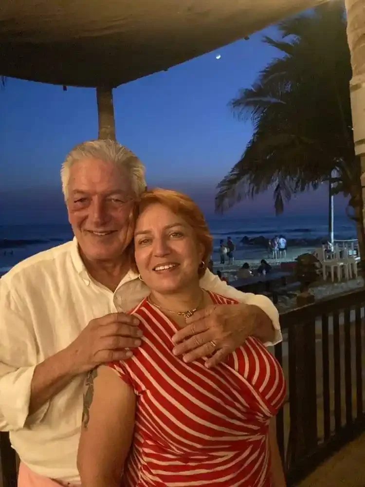 Inga and Randy stand together on a beachfront terrace in Mazatlán at dusk, the Pacific behind them under a darkening blue sky.
