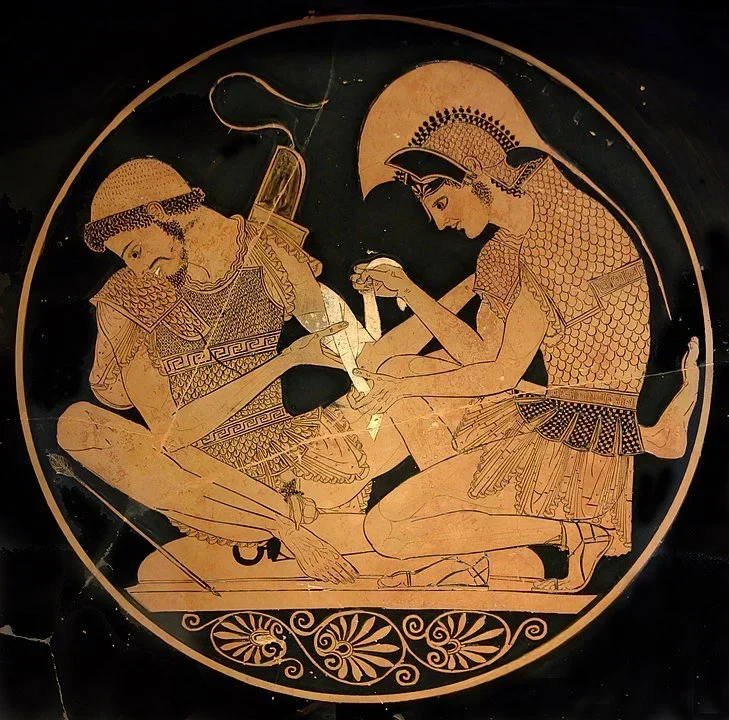 Red-figure Greek kylix interior showing Achilles seated, bandaging the wounded arm of Patroclus, both figures in profile.