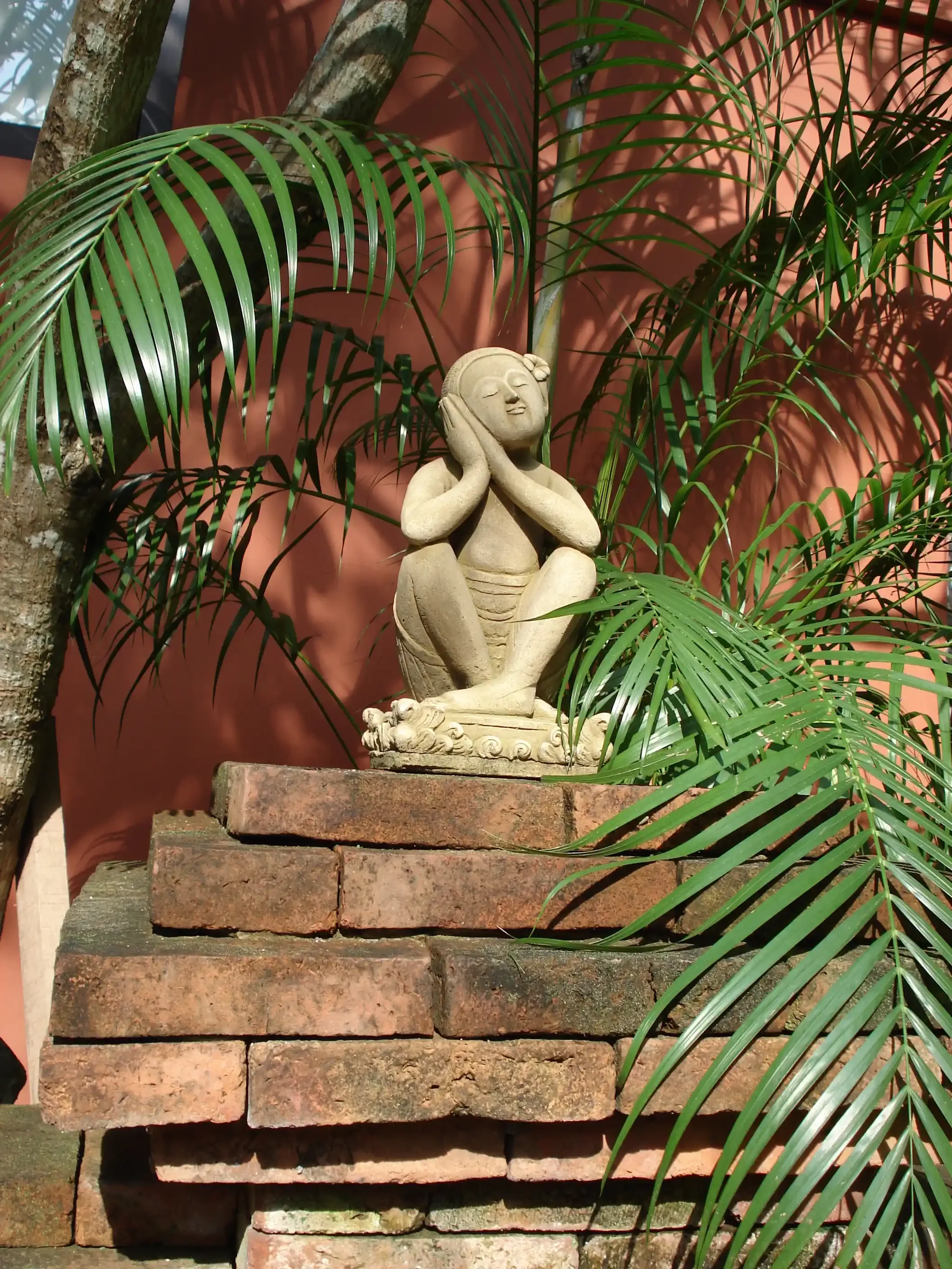 A carved stone figure resting its head on its hands on brick garden steps