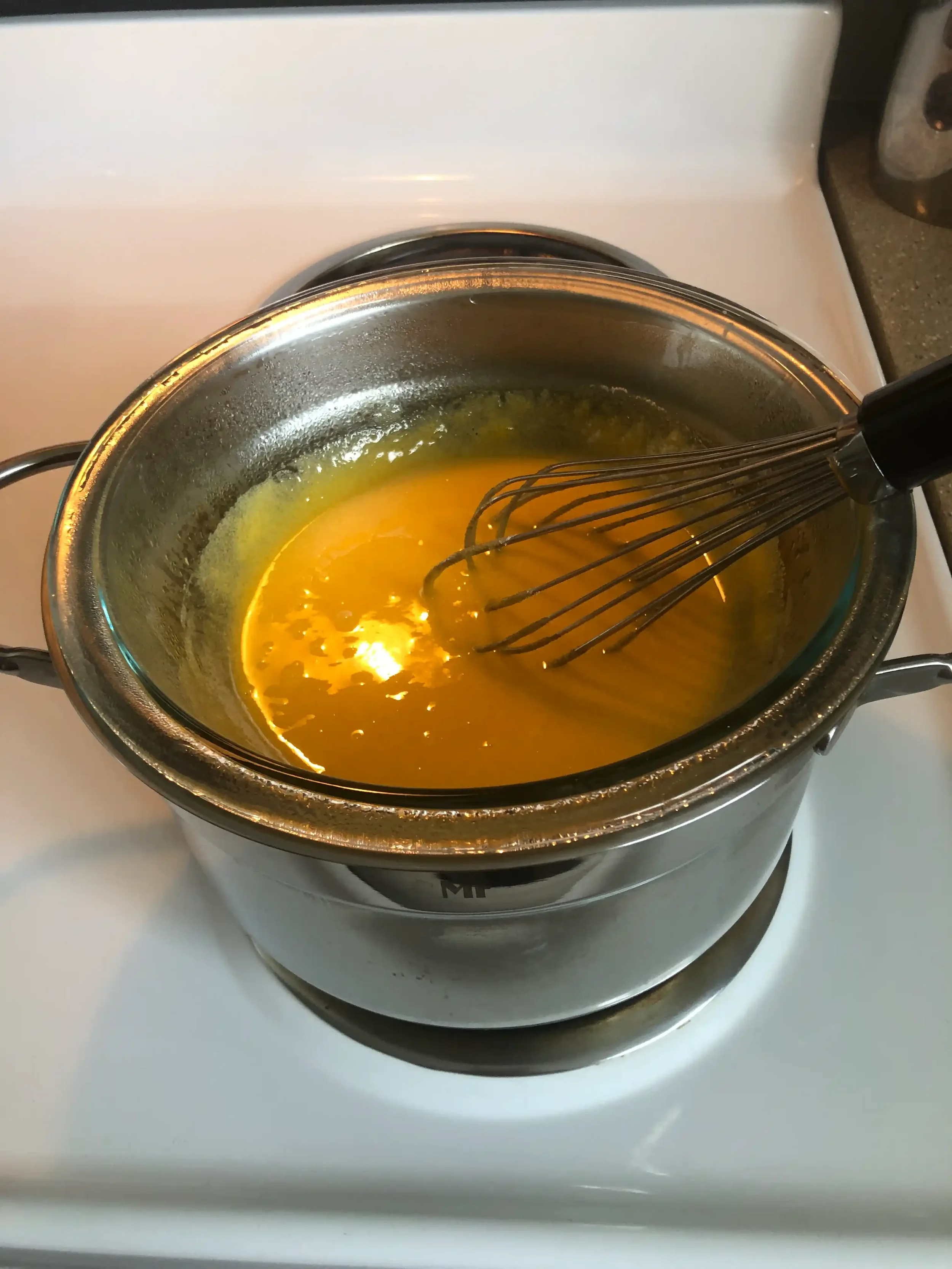 A glass bowl of pale, ribboning sabayon being whisked over a pot of simmering water in place of a bain-marie.