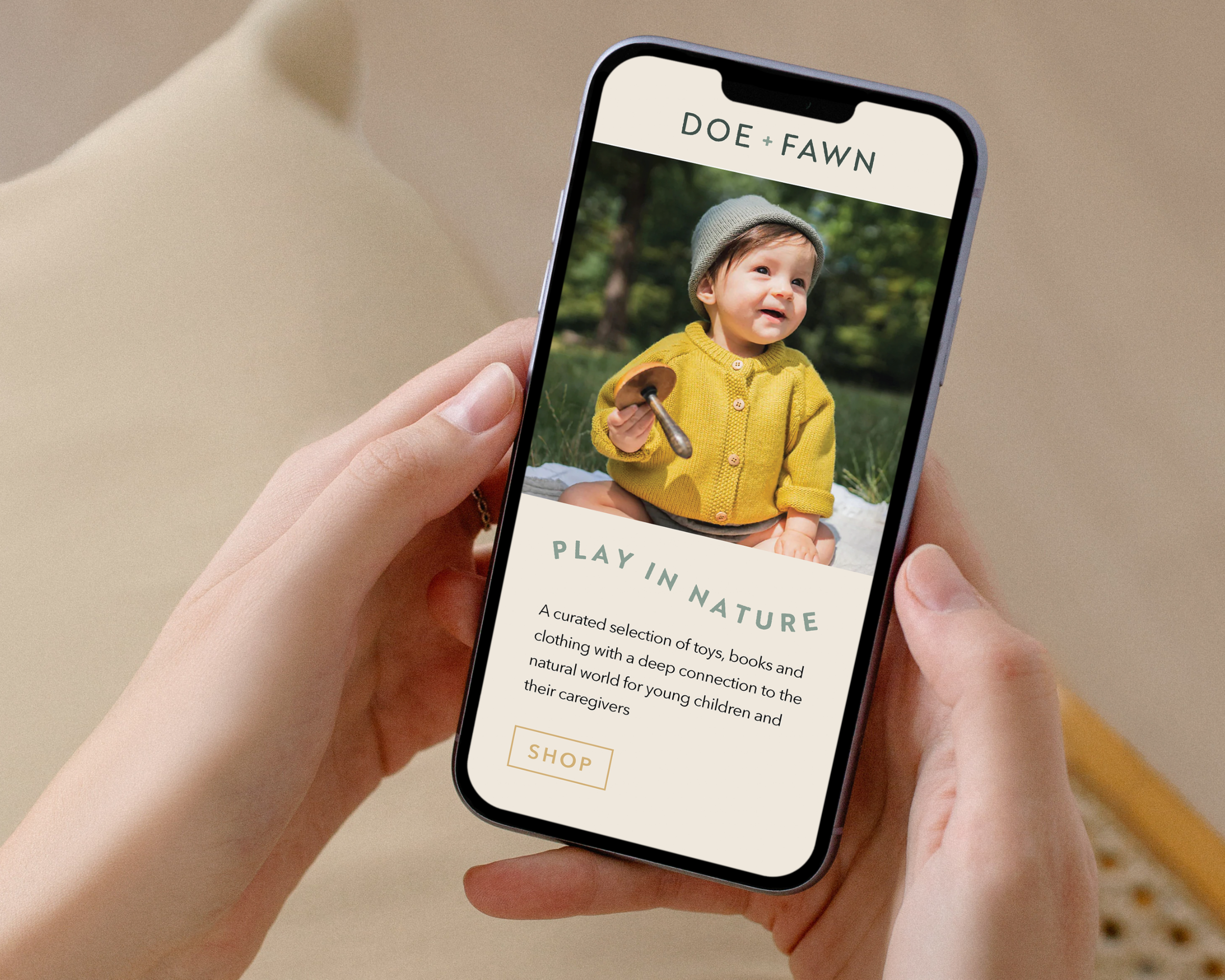 Close-up of a person holding a smartphone displaying a website titled 'DOE + FAWN' with a picture of a young child in a yellow sweater and gray beanie, outdoors with greenery.
