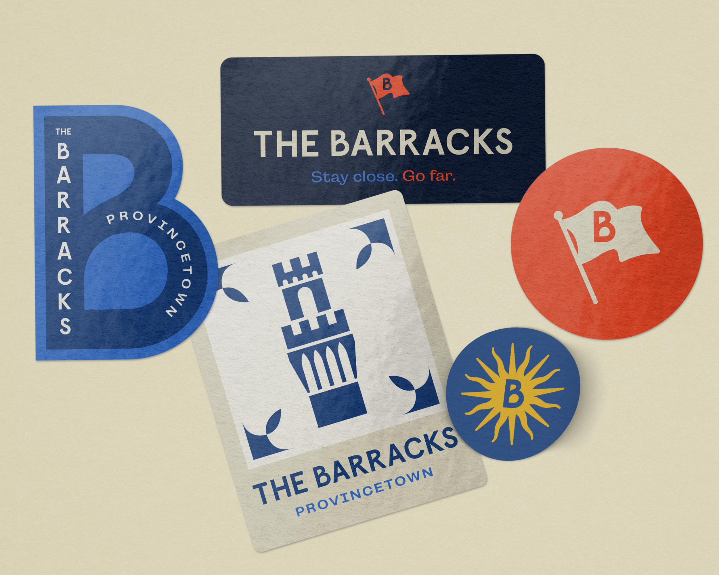 Collection of stickers and cards from The Barracks in Provincetown, including a blue circular sticker, a dark blue rectangular sticker with a red flag, a white card with blue and red text, and a red circular sticker with a white flag and red 'B'.