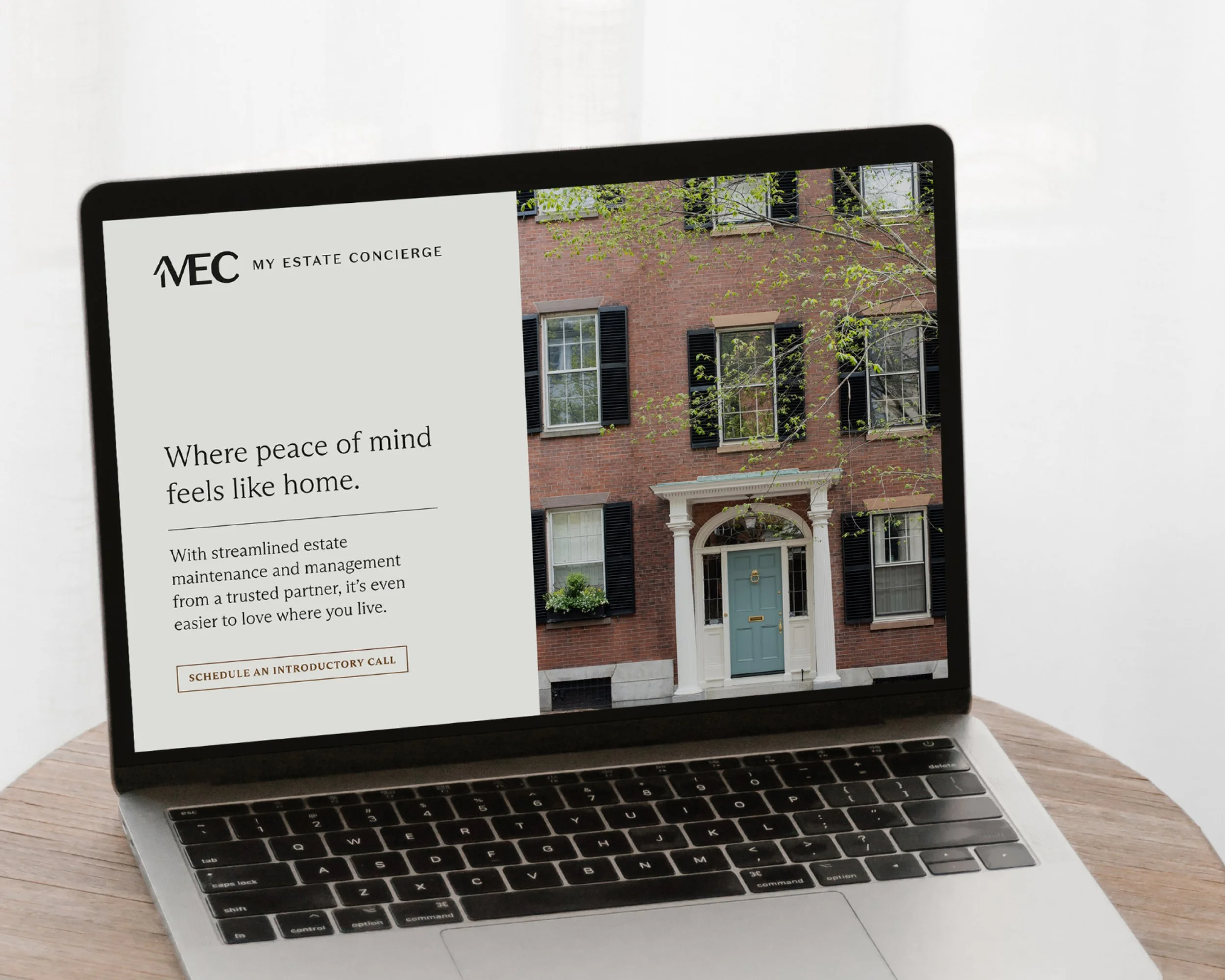 A laptop displaying a website for MEC My Estate Concierge, with an image of a brick house with black shutters and a teal front door, and some green trees in the background.