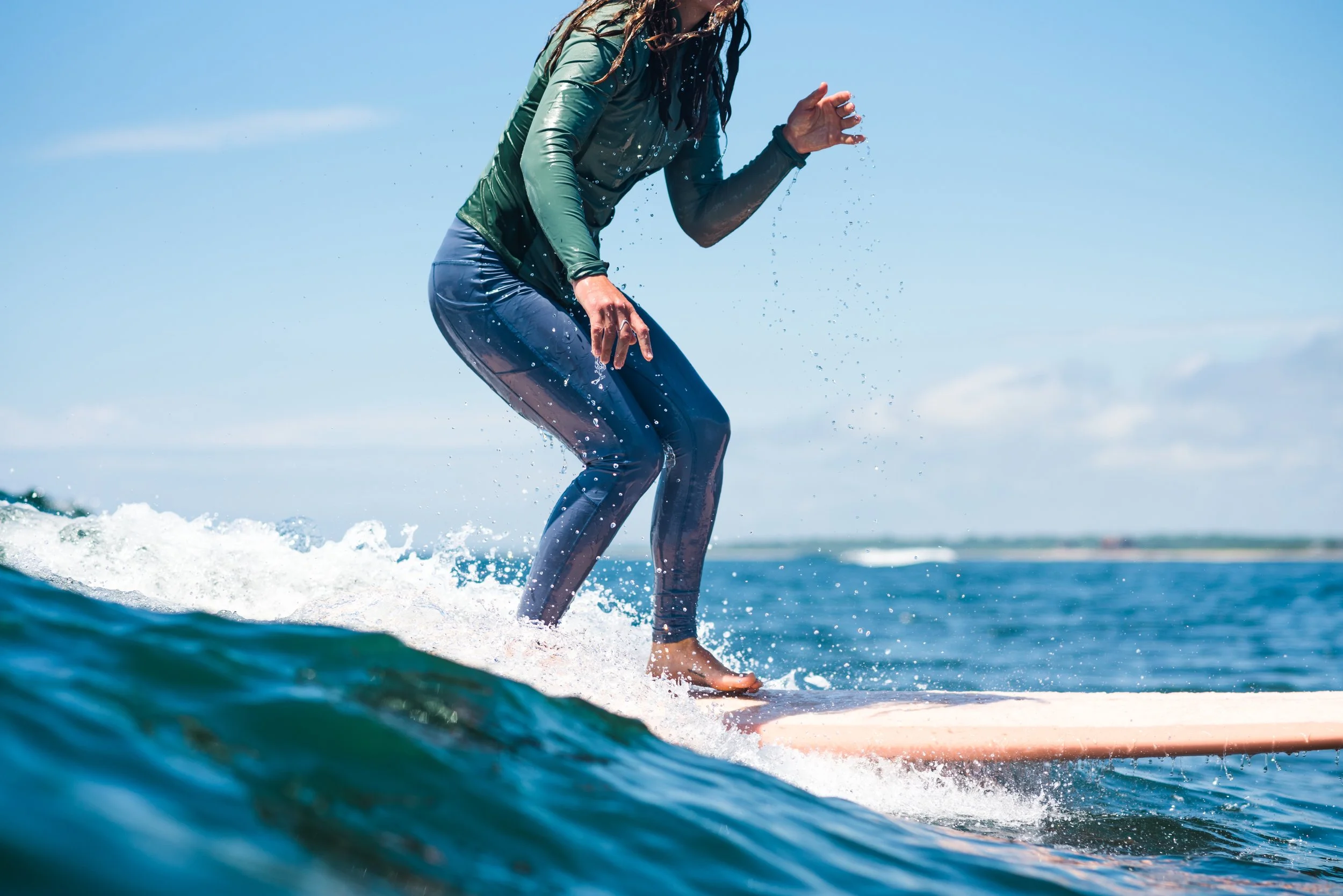 Person riding a surfboard on the ocean waves during daytime, wearing a wetsuit, with water splashing around.