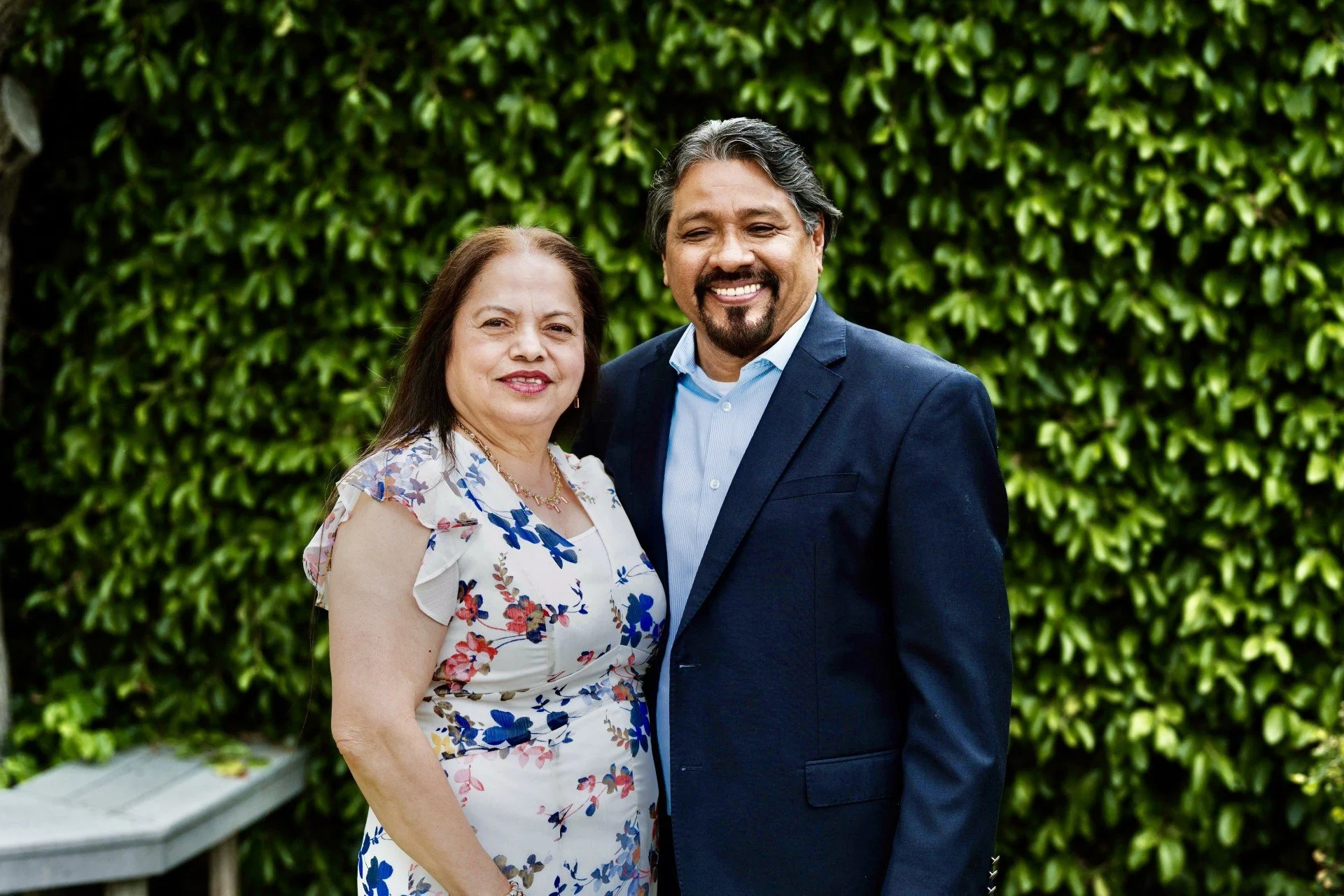 A man and a woman posing in front of greenery and smililing