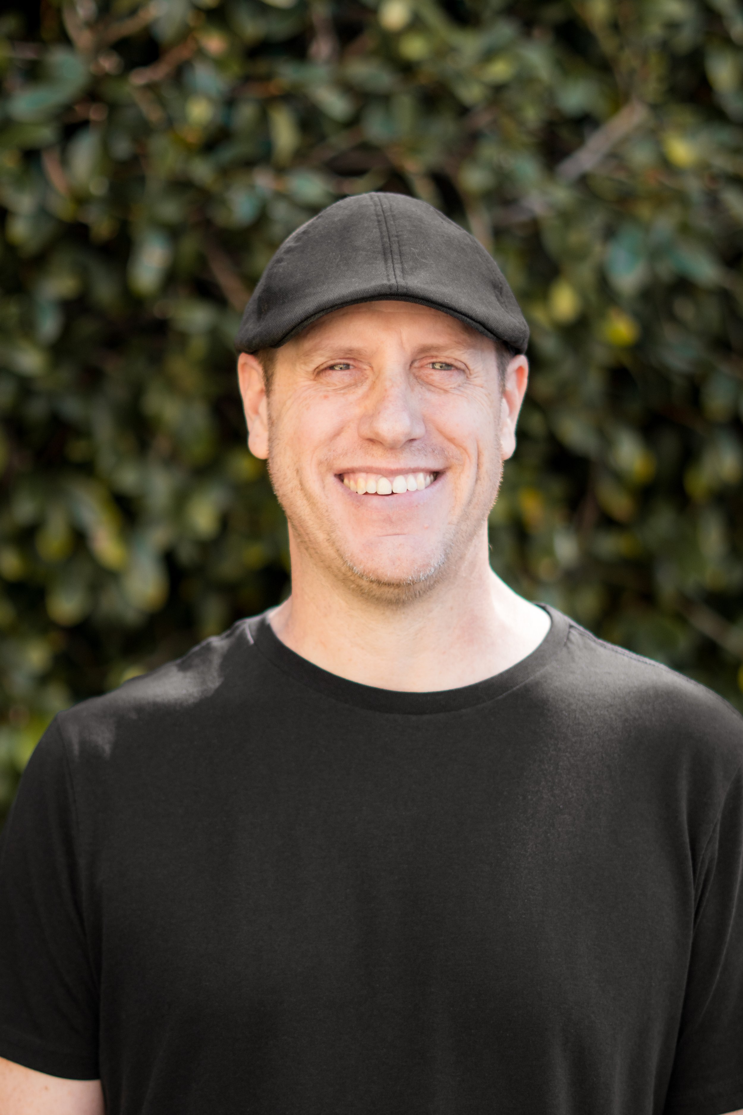 Smiling man in casual shirt and black cap outdoors