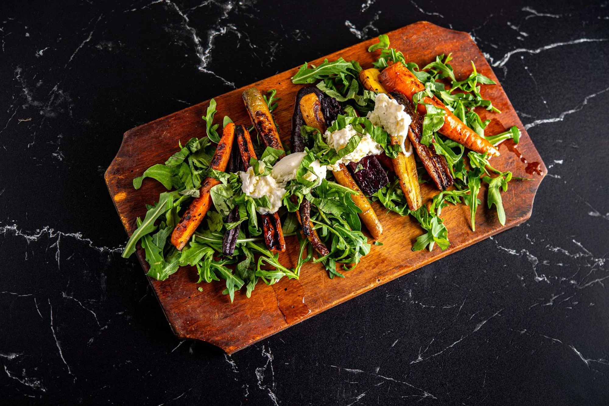 Grilled vegetable salad with carrots, eggplant, and greens on wooden serving board.