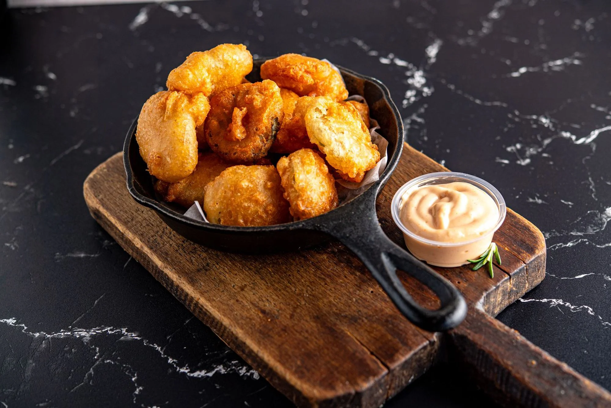 Bowl of fried chicken pieces with a side of dipping sauce on a wooden platter.