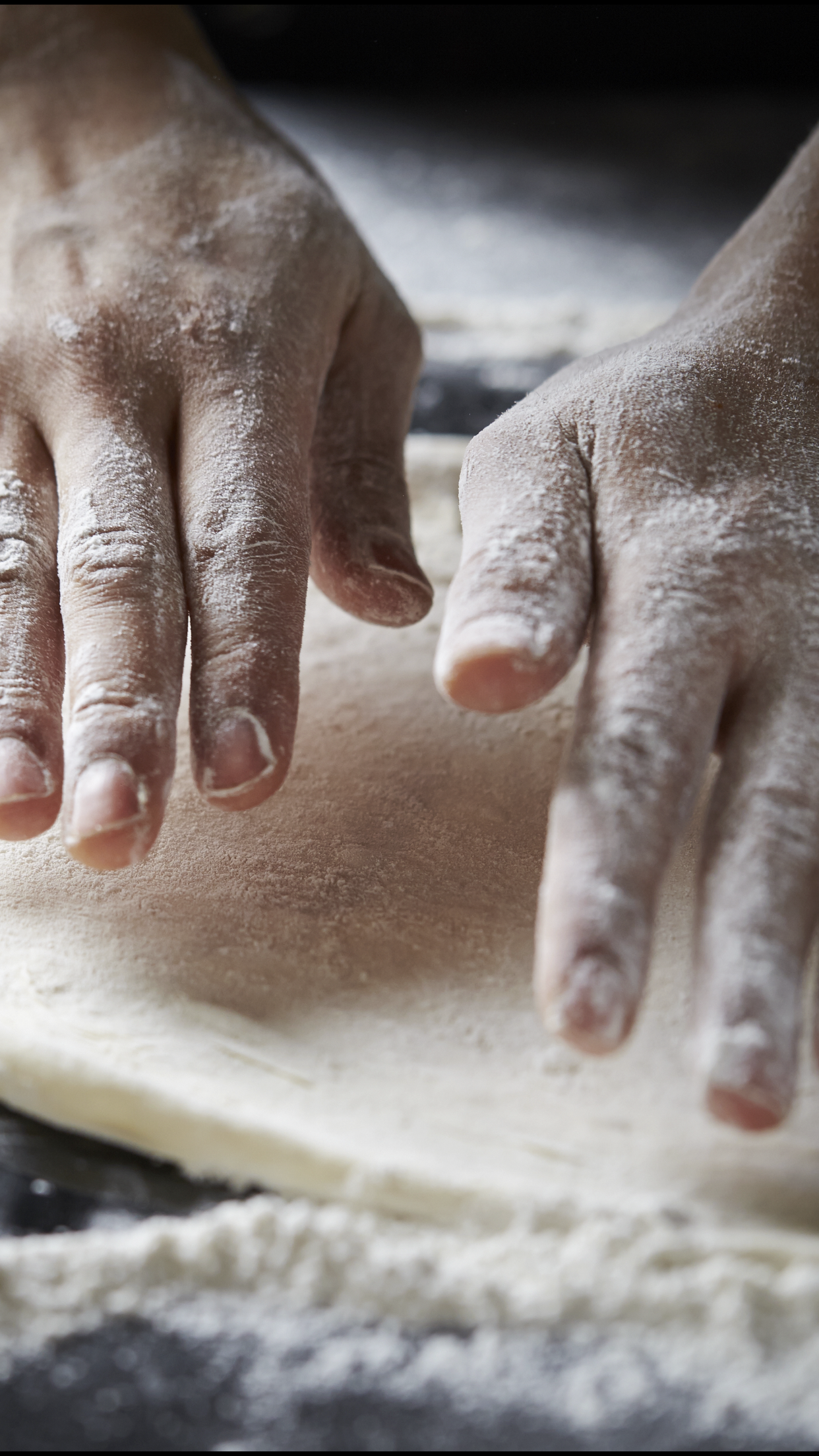 Hands dusted with flour rolling out dough on a surface.