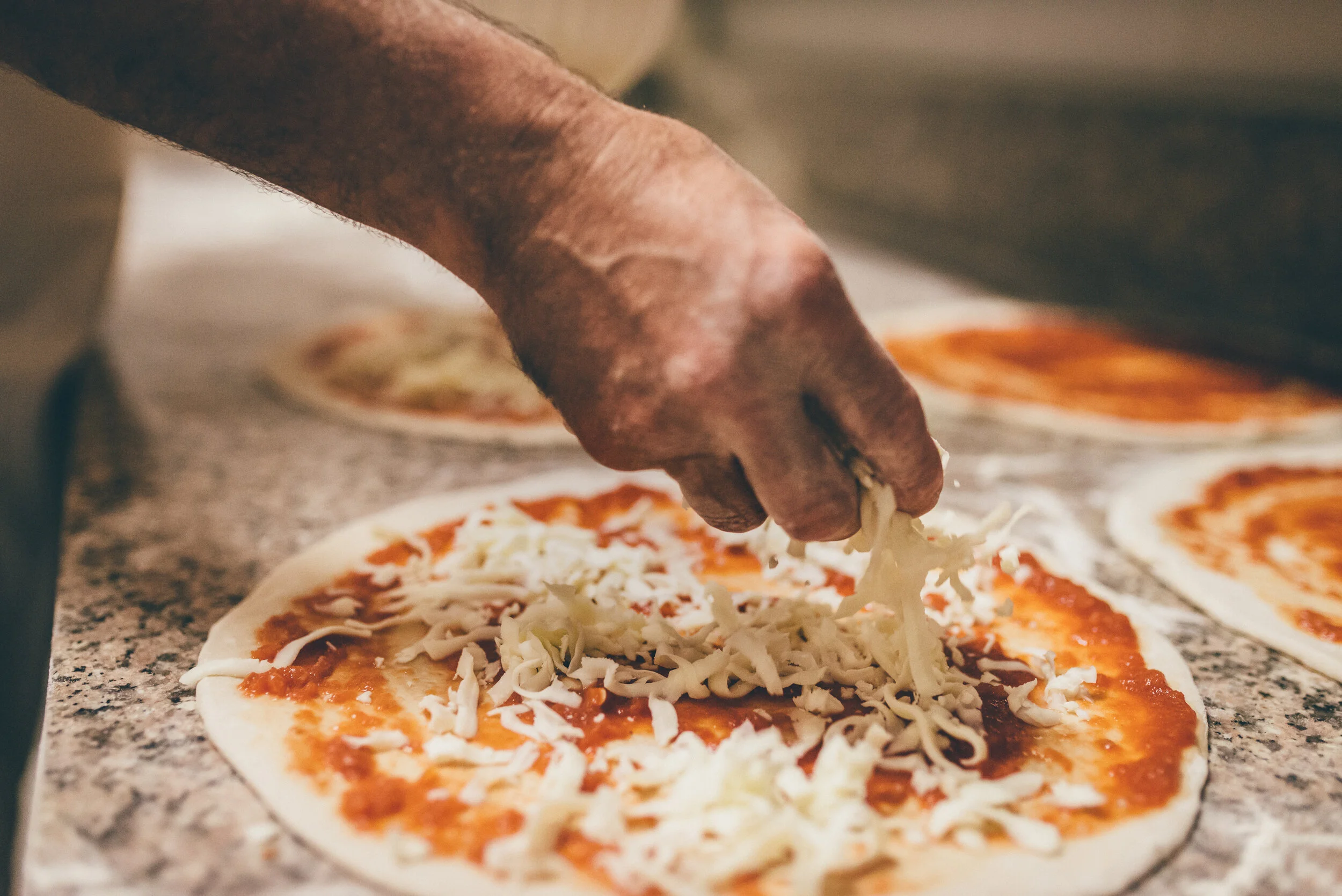 Close-up of a hand sprinkling shredded cheese onto a pizza before baking.