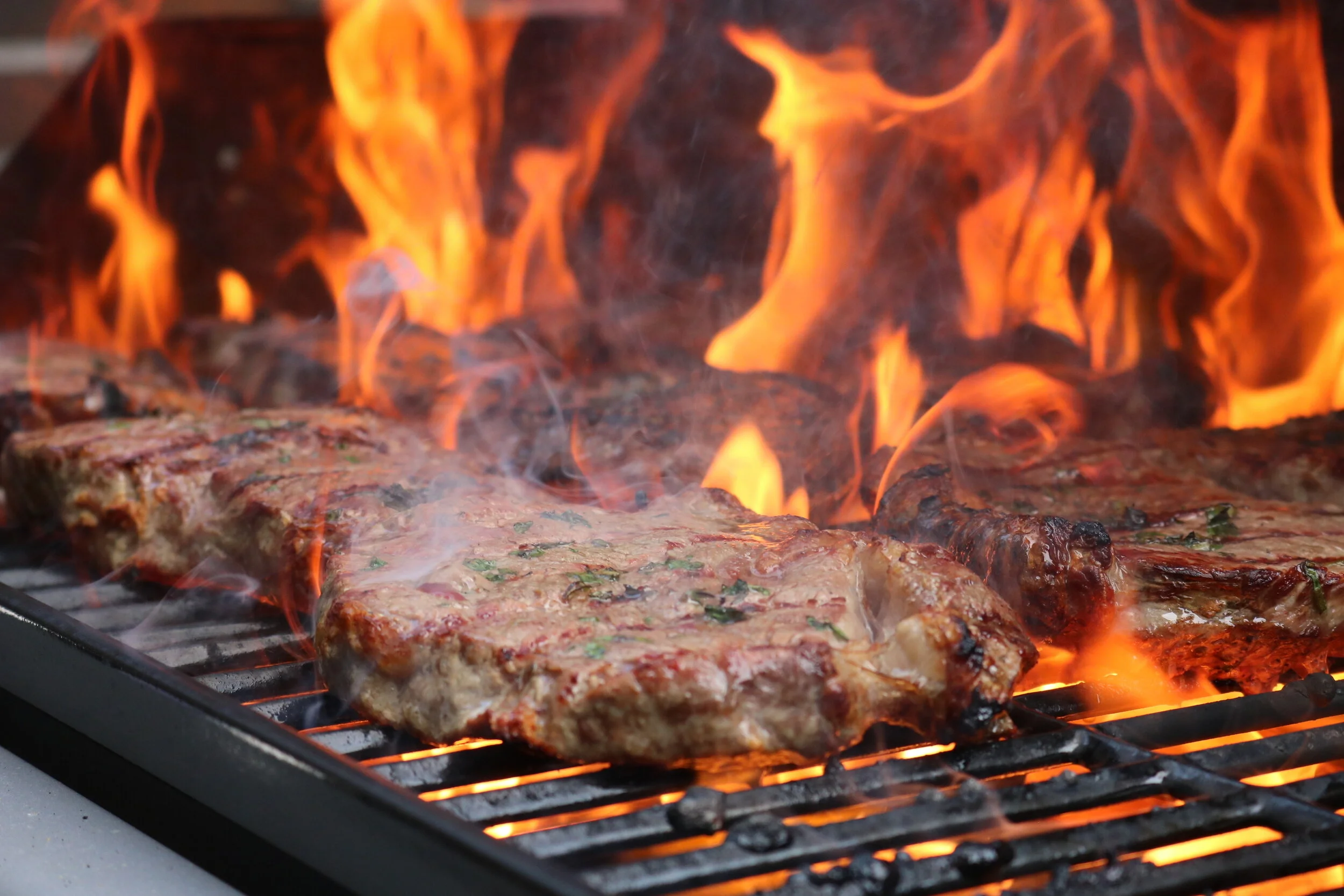 Steaks grilling on an outdoor barbecue with flames and smoke.
