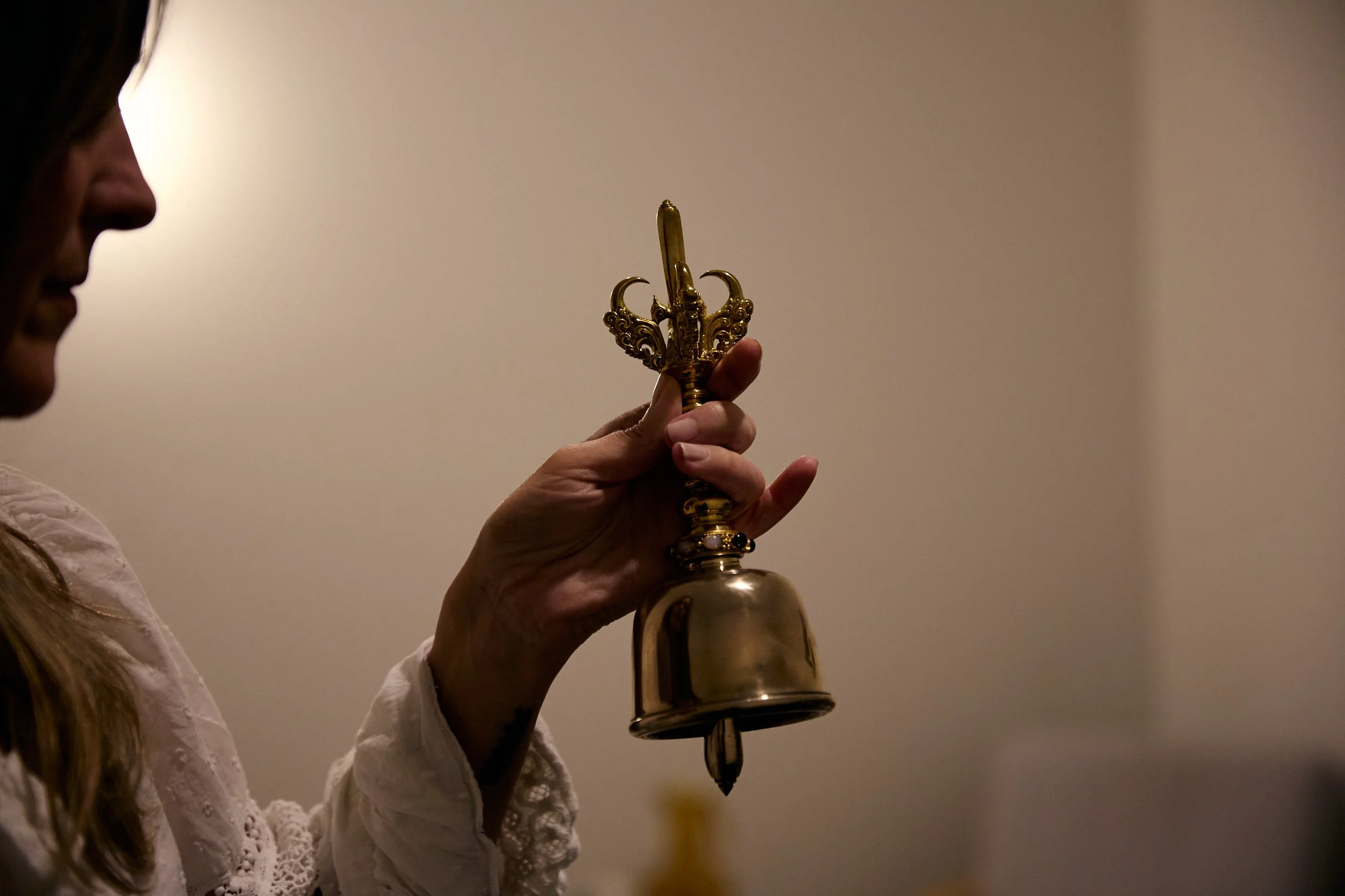 A woman holding a small gold religious bell with a decorative handle.