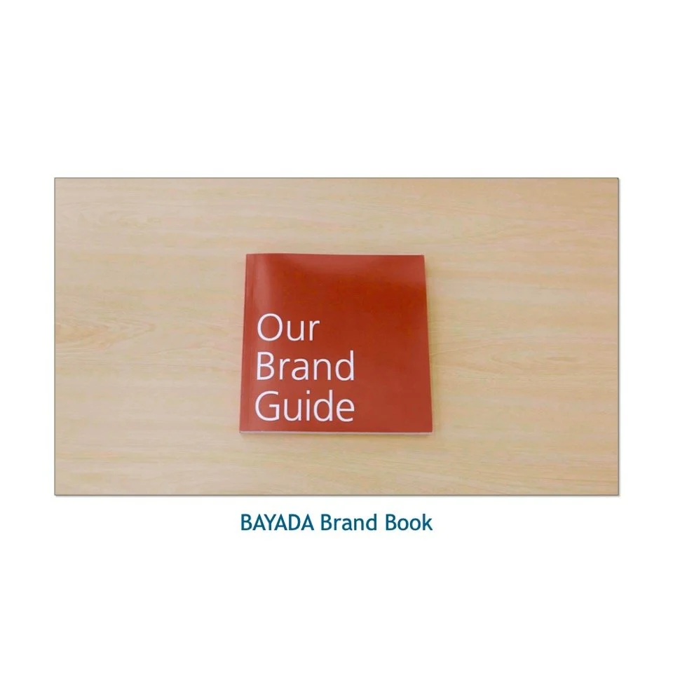 A red booklet titled 'Our Brand Guide' placed on a light wooden surface with the text 'BAYADA Brand Book' below.