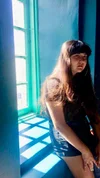 a japanese-mexican femme sitting by the window, lit by the blue hue coming in through the window.