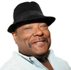 a smiling black man in a black fedora, smiling in front of a white background