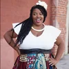 a beautiful black woman slaying with her long braids falling over her right shoulder, a white flower on her head matching her white top, her hands on her hips