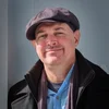 a happy white man in a hat, a closed mouth smile on his face