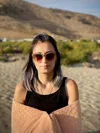 a beautiful mexican woman standing on the beach, shades on, a towel wrapped around her arms.