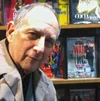 an older jewish man standing in front of a copy of War Inc in a bookstore
