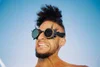 a black male wearing steampunk glasses with his hair tied high, grimacing