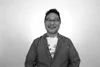 a black and white photo of a smiling asian man with glasses wearing a jacket in front of a white backdrop