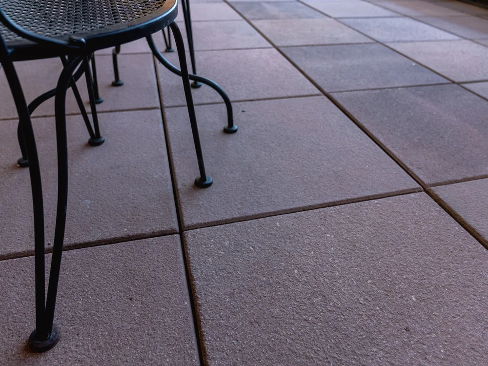 Part of a black metal outdoor table and chair on a tiled patio.