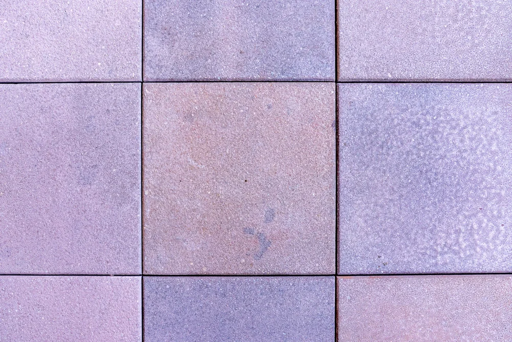 Close-up of a tiled concrete floor with nine square tiles in shades of purple and pink.